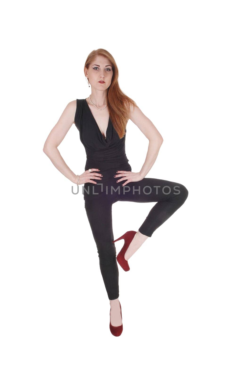 A beautiful brunette woman in a black outfit and high heels standing.on one leg, looking serious, isolated for white background.