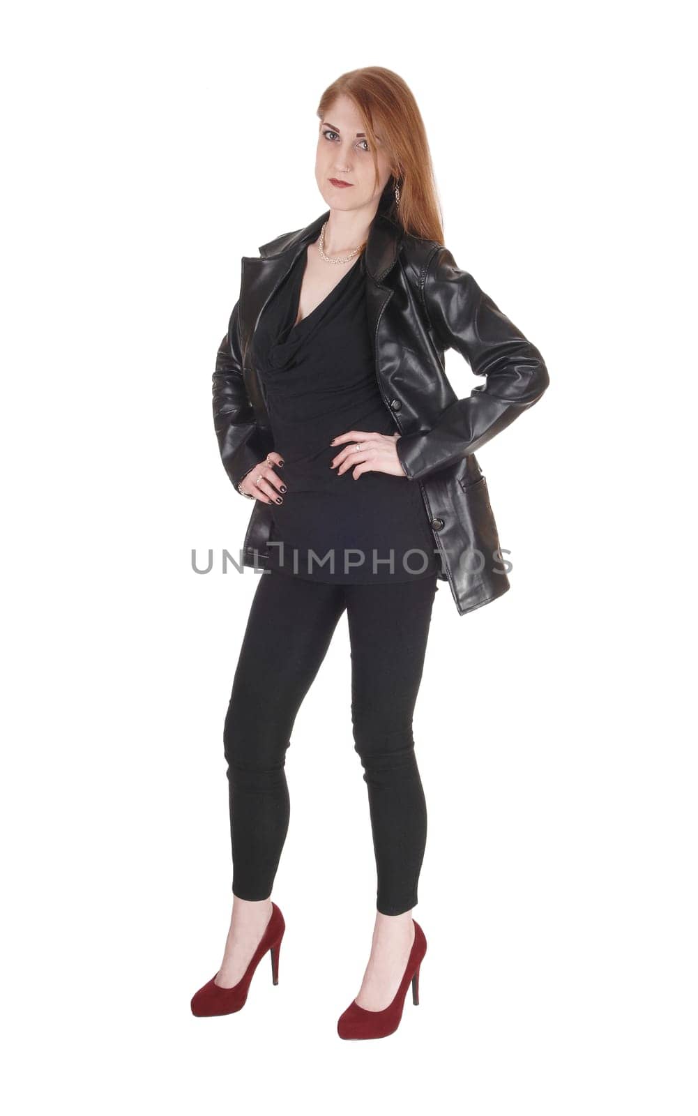 A beautiful serious looking woman standing in black leggings and a.black leather jacket and heels, isolated for white background.