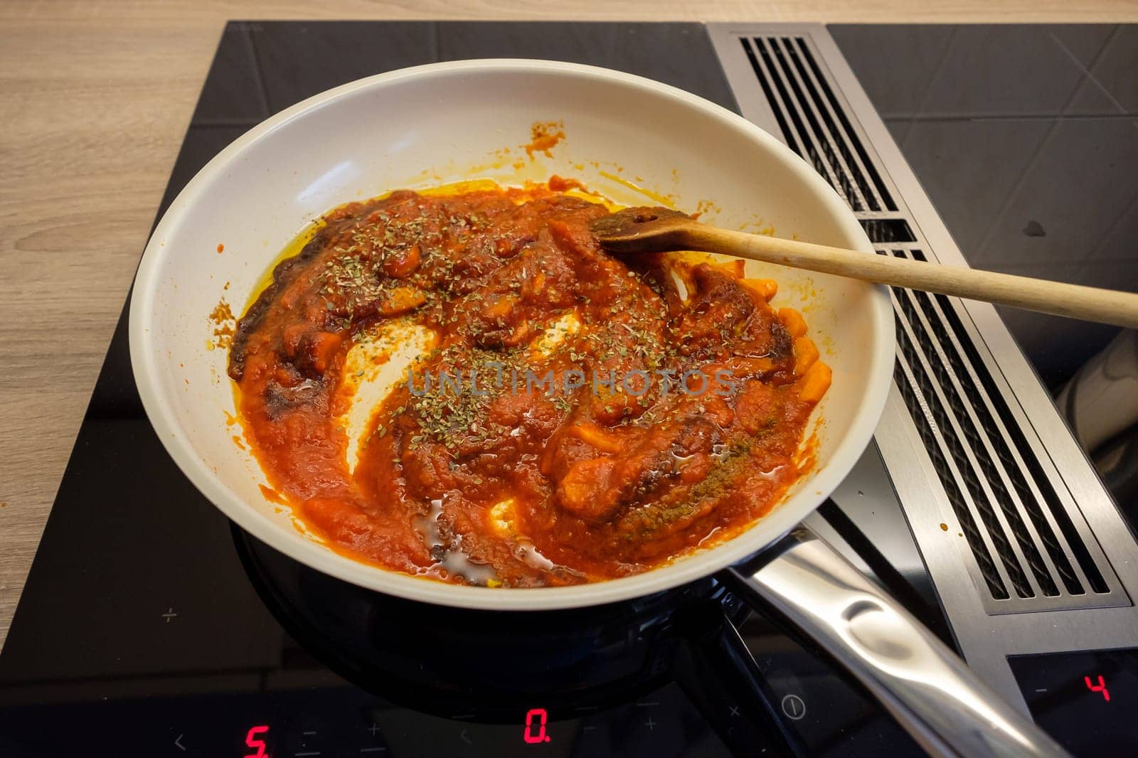 Frying pan on stove with cooking spoon and tomato sauce with oregano