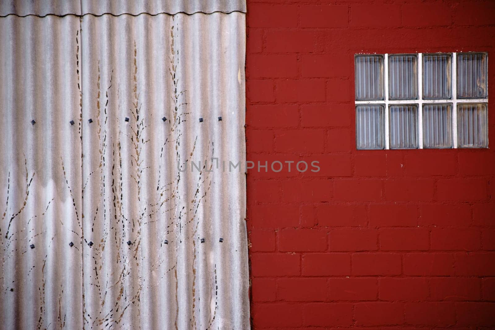 The close-up of a window made of glass tiles on a red painted wall with adjacent corrugated iron.