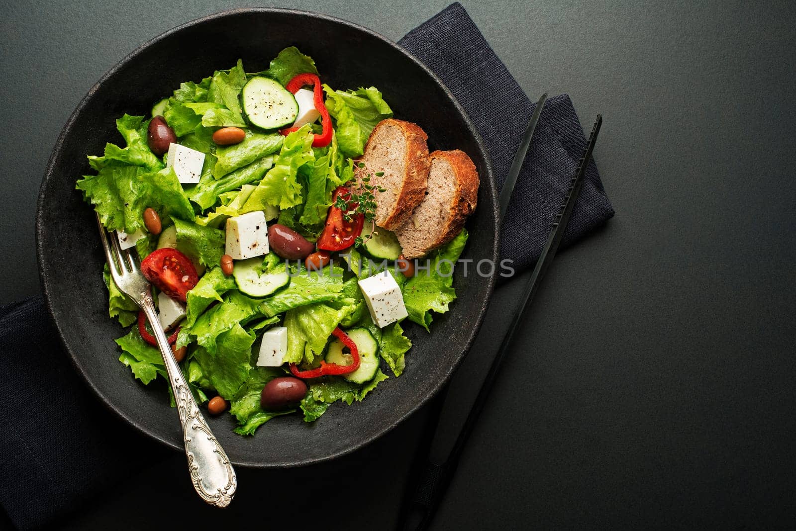 Green salad with cheese and fresh vegetables on a black background. Greek salad.