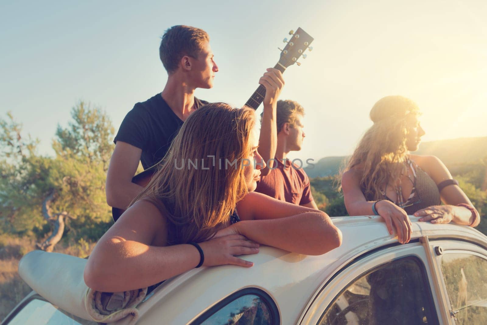 Group of happy people in a car at sunset in summer.