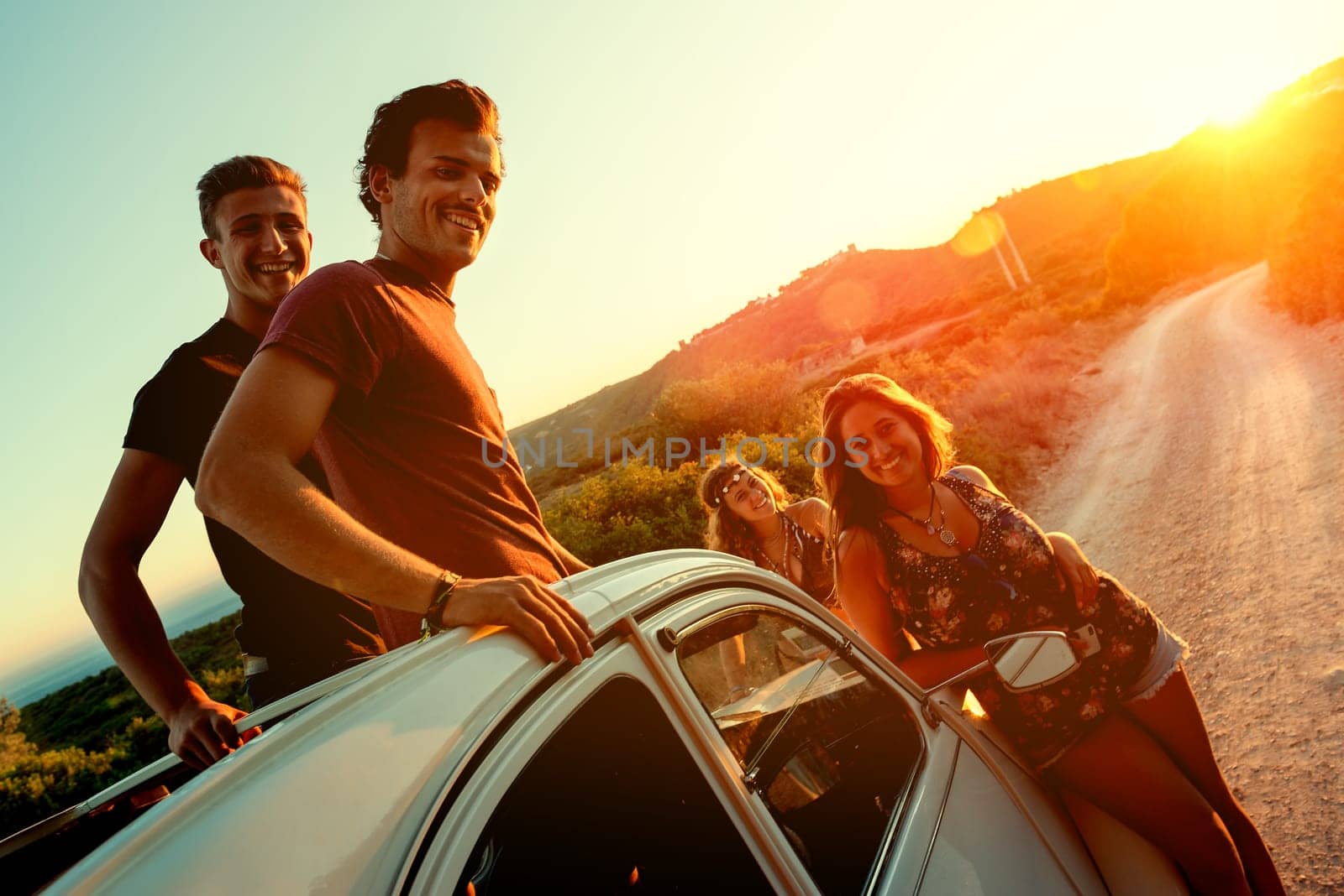 Group of happy people in a car at sunset in summer.