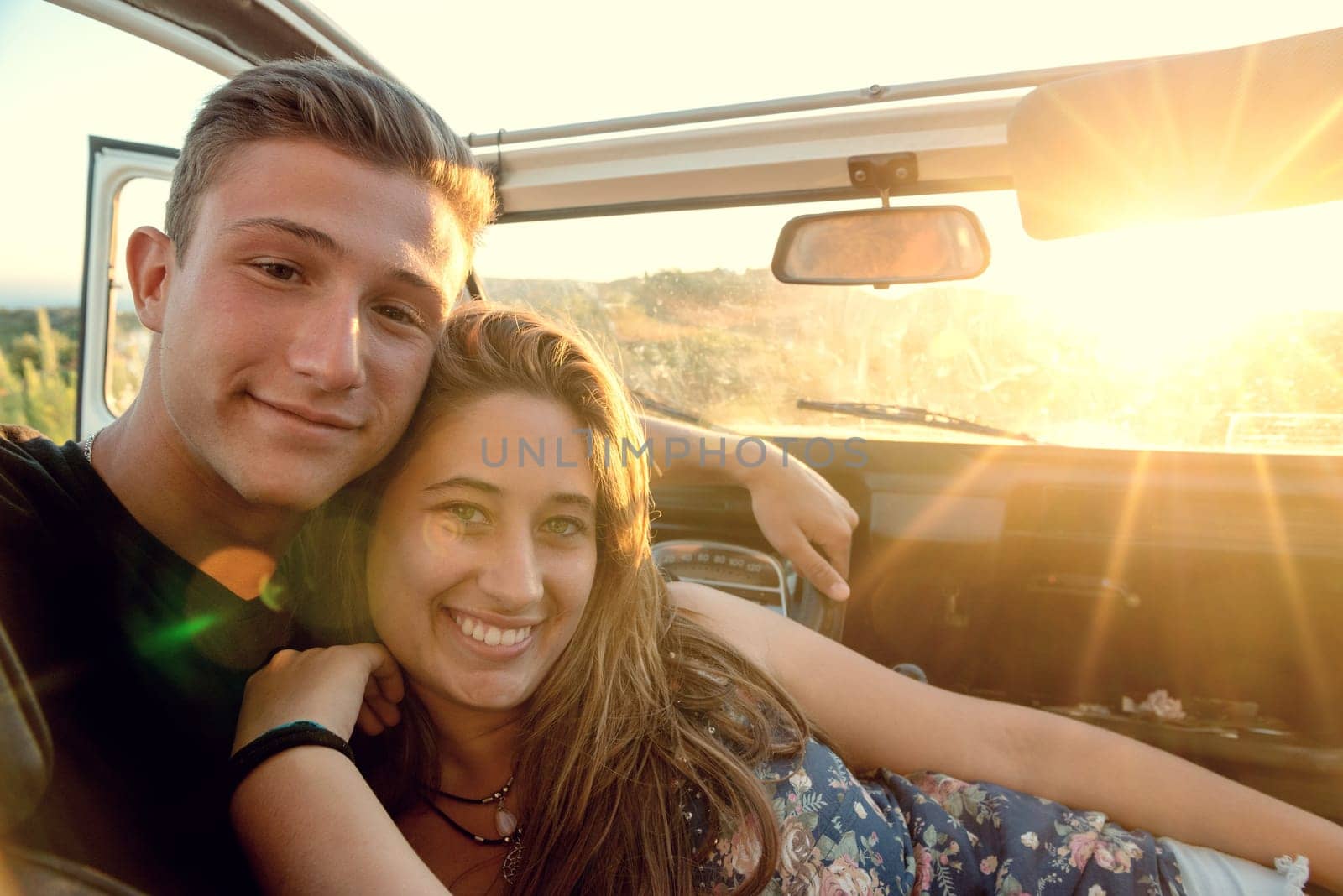 Happy young couple in a car enjoying the beautiful sunset in countryside.