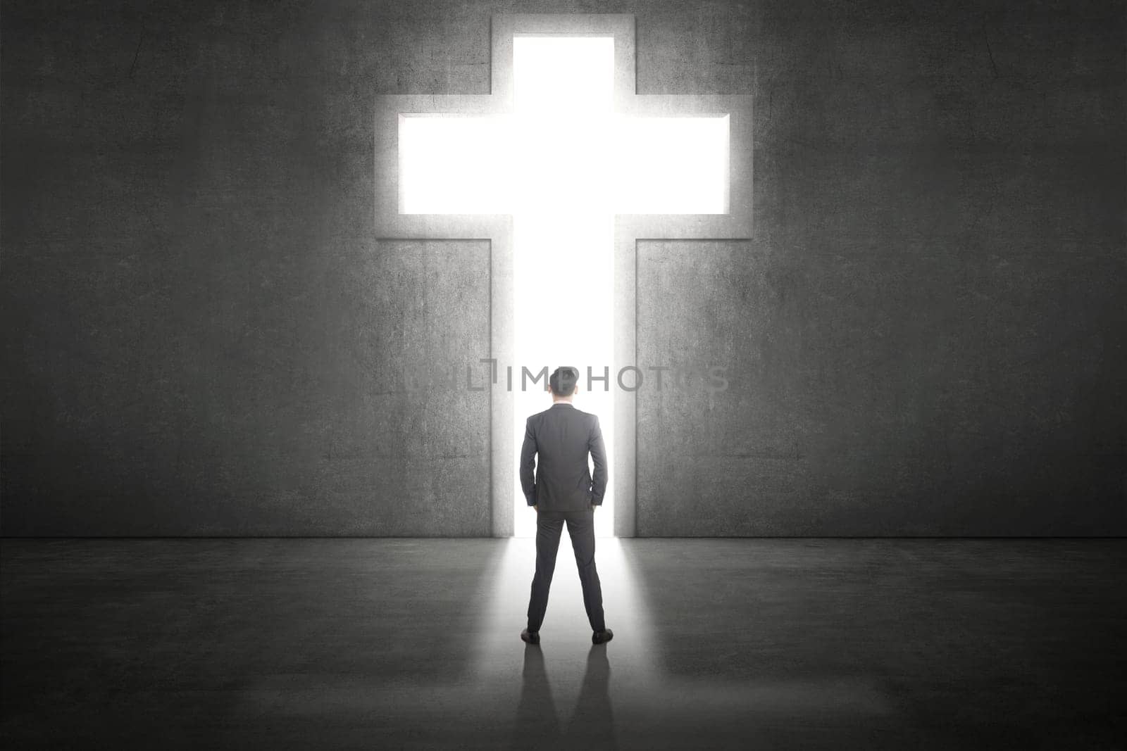Business man standing in front of the shining cross on the wall