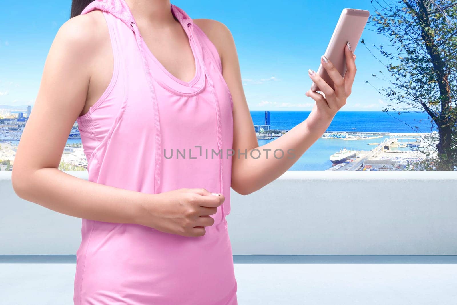 Close-up of asian sporty woman using mobile phone on terrace with cityscape and sea background