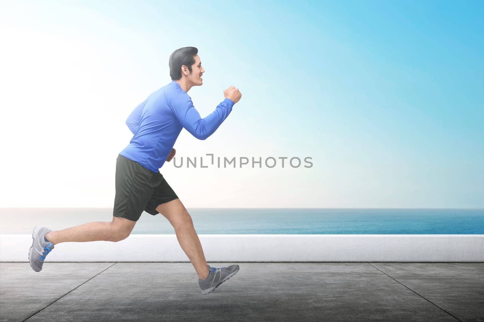 Young asian man in sportswear running on terrace with ocean background