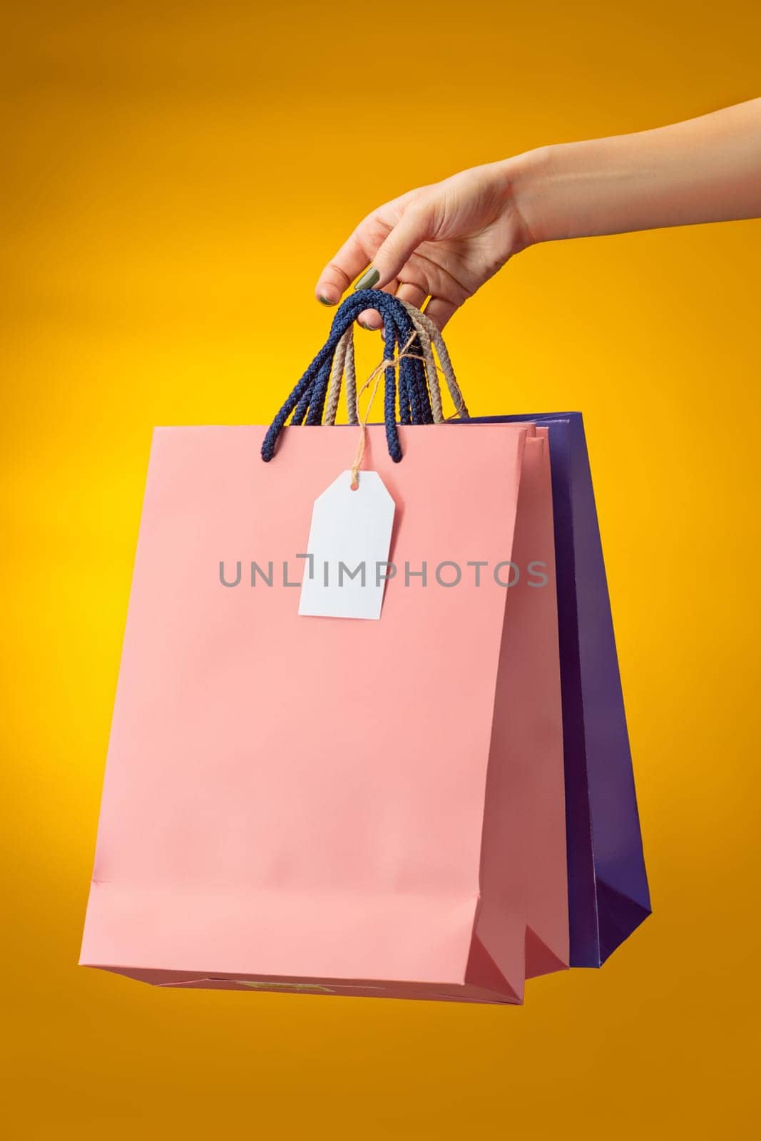Female hand holding bright shopping bags on yellow