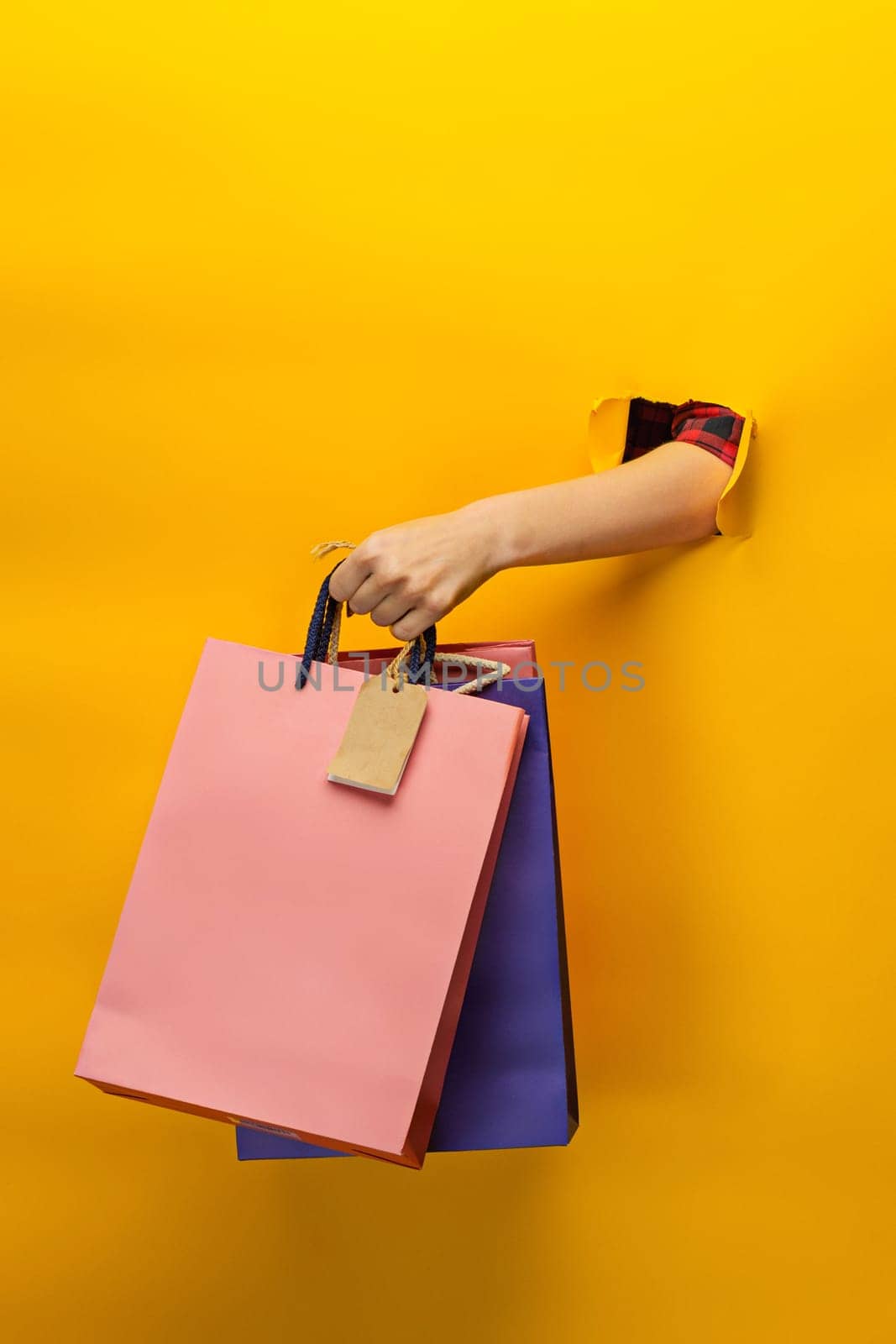 Female hand holding bright shopping bags on yellow