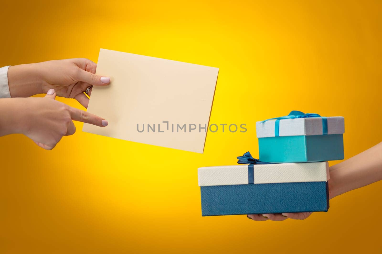 The closeup picture of man and woman's hands with gift box on yellow background with copy space on empty blank