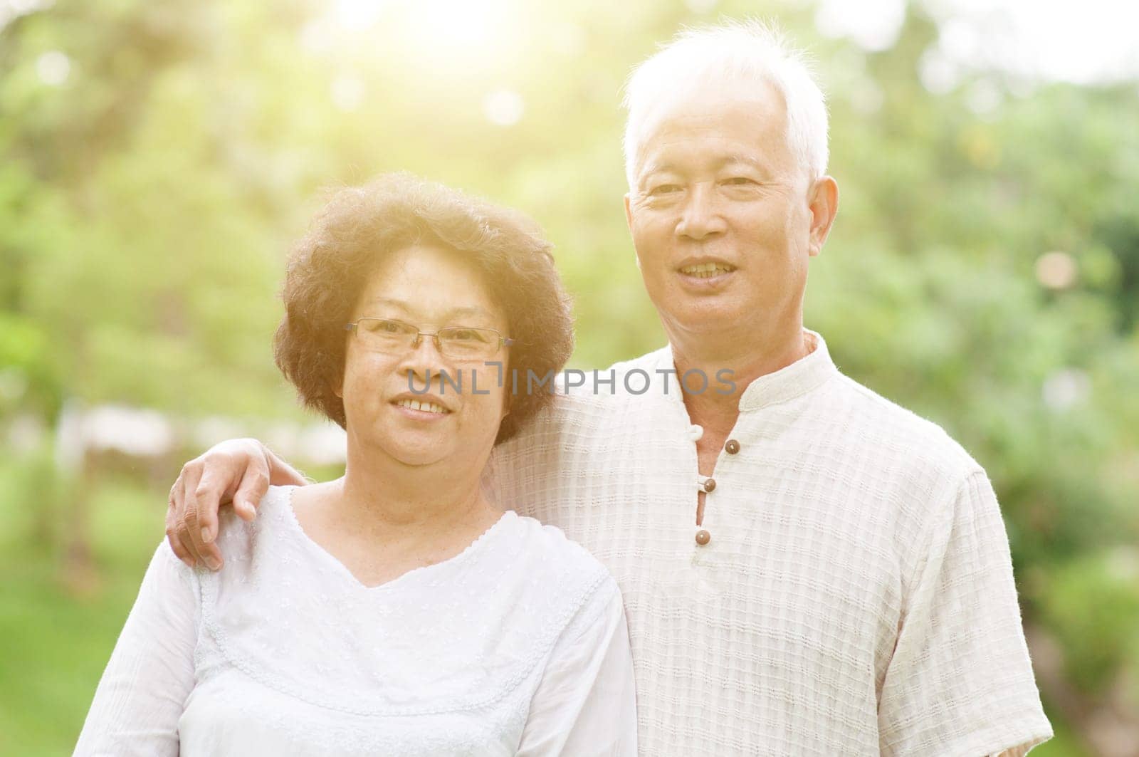 Happy Asian elderly couple smiling at outdoor park on a sunny day.