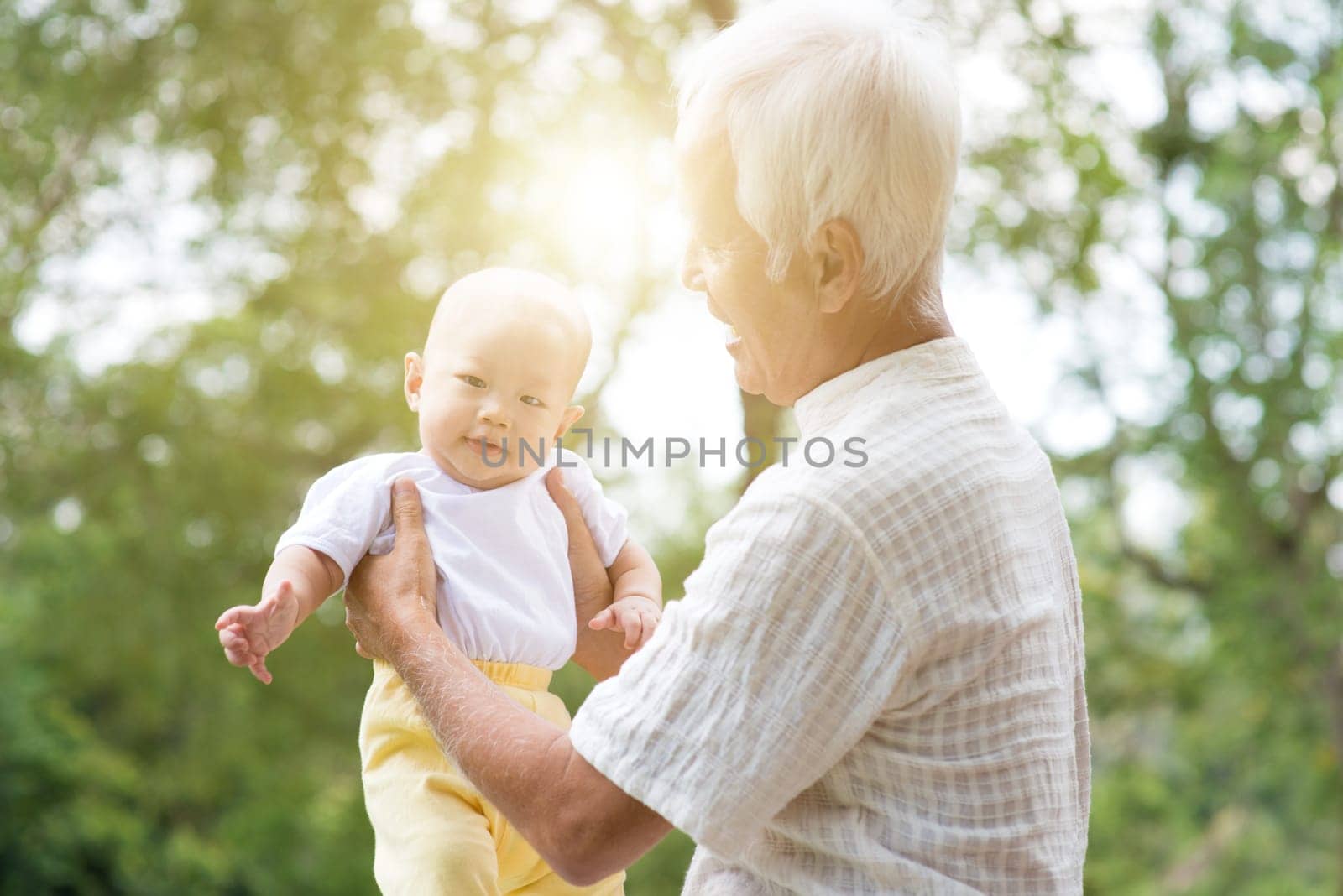 Grandfather taking care of baby grandchild in outdoor park. Asian family, life insurance concept.