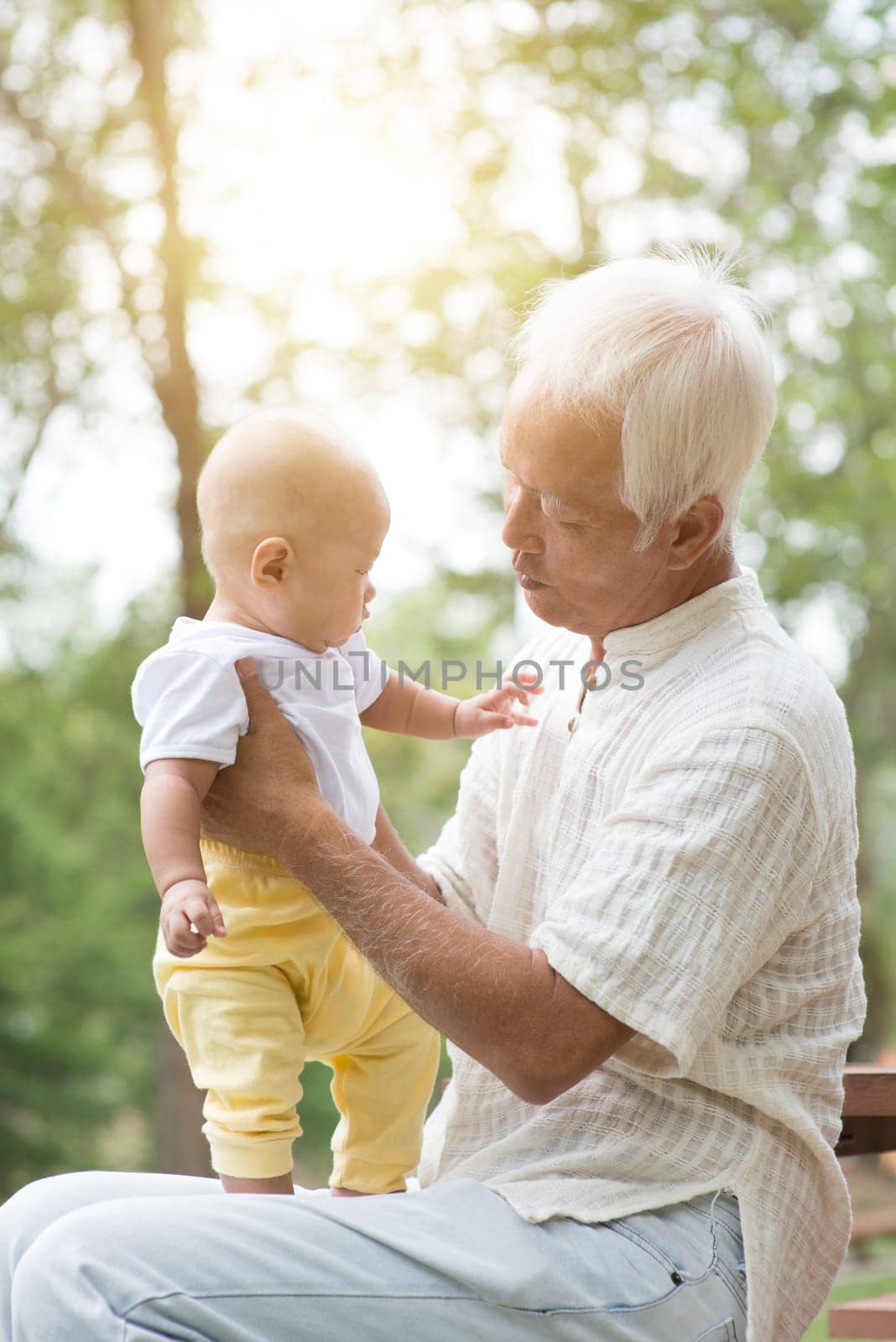 Happy grandfather playing with grandson, Asian family at outdoor park.