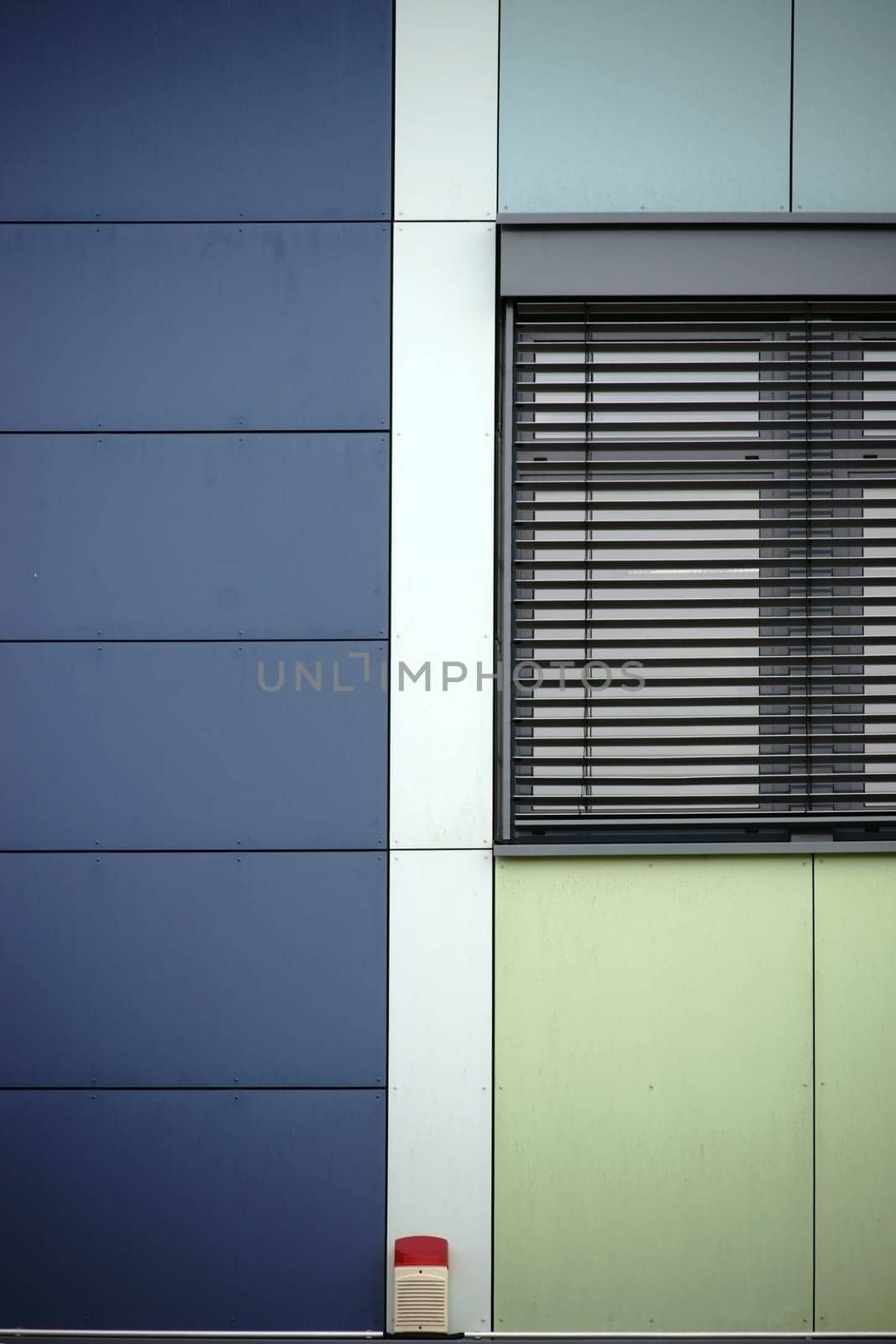 The modern façade of a modern residential building with a metal window with metal blind and a warning light.
