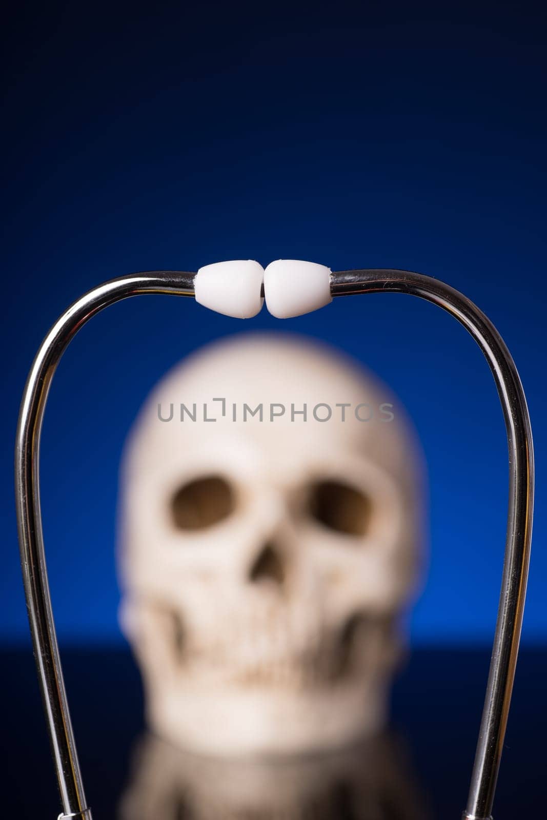 Stethoscope i focus and blurry skull isolated on black blue background
