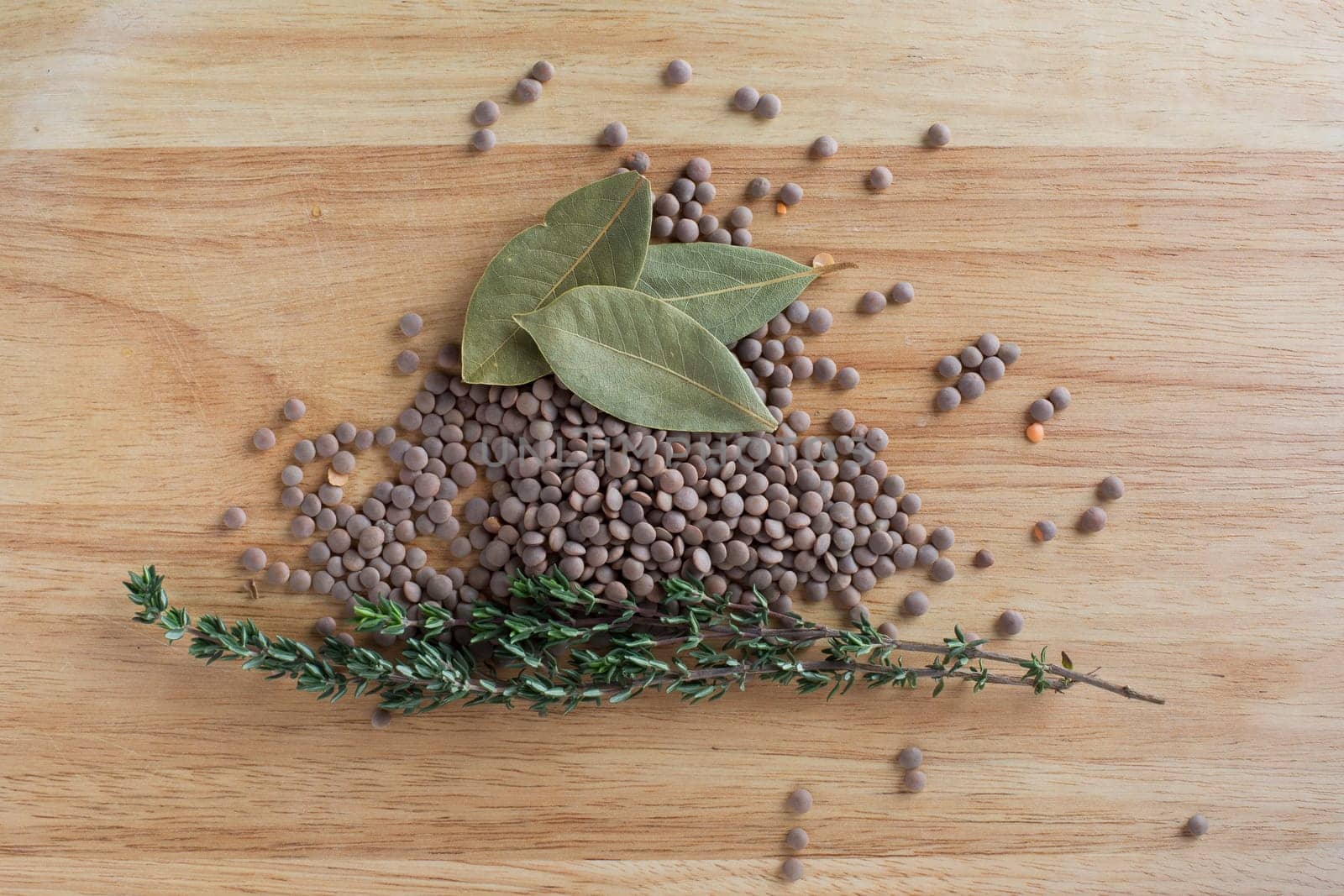 Lentils, thyme and bay leaves on wooden board from directly above.