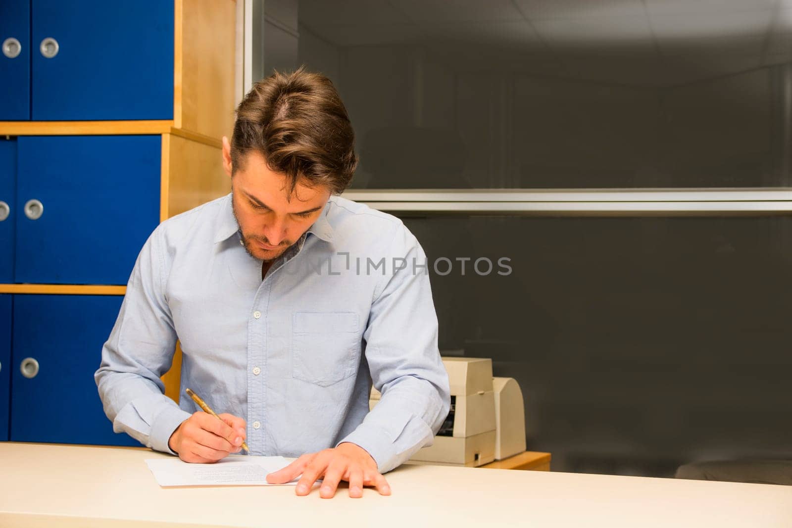 Man sitting working in an office concentrating looking down while writing with a pen on a sheet of paper