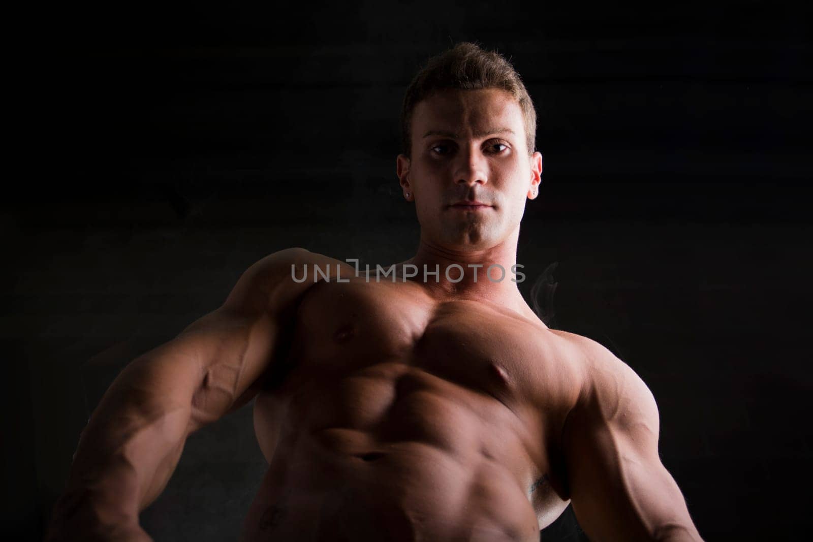 Handsome shirtless bodybuilder shot from below. Close-up of ripped sexy abs and pecs