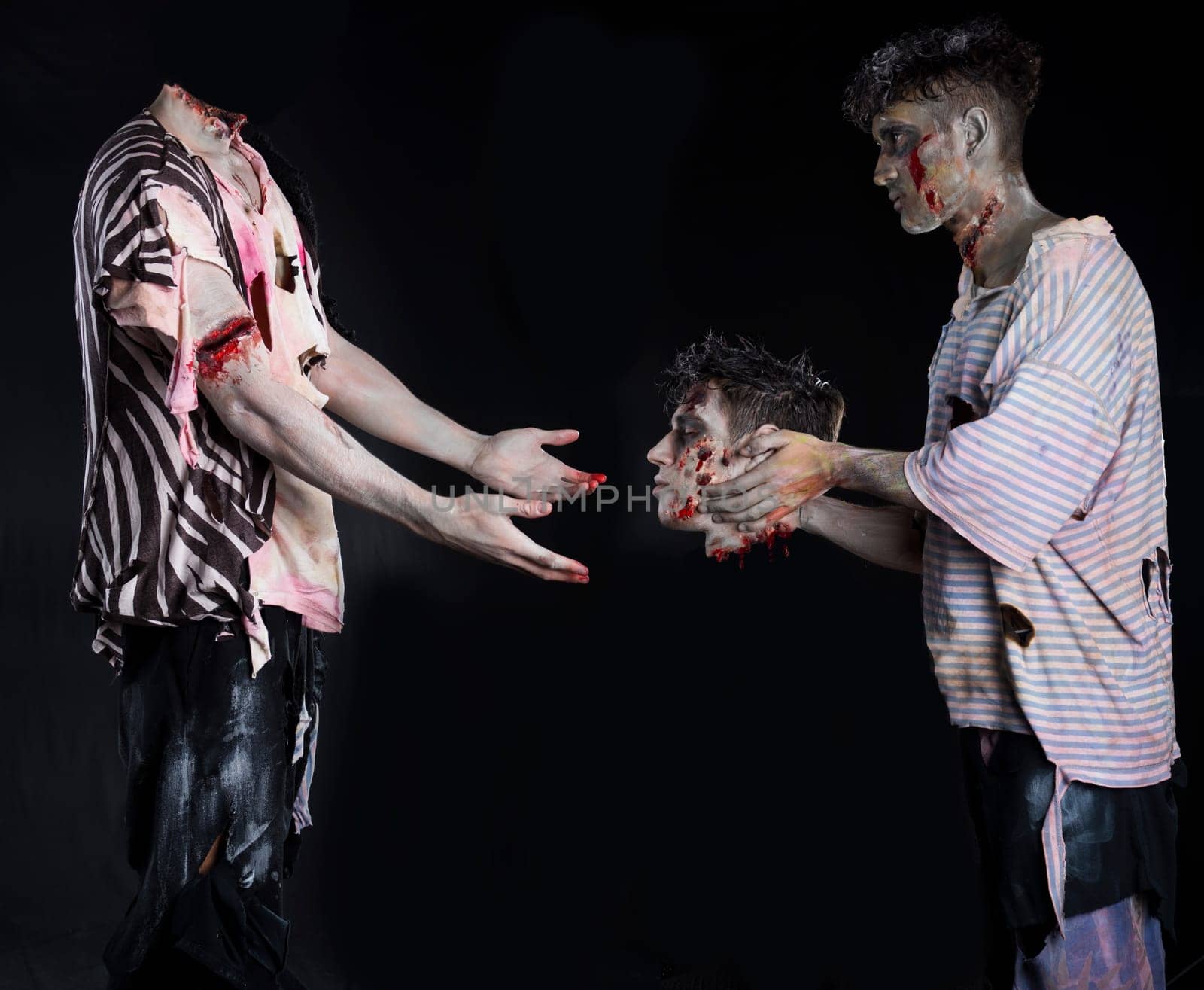 Two male zombies, one giving the head to the decapitated one's body, standing on black background