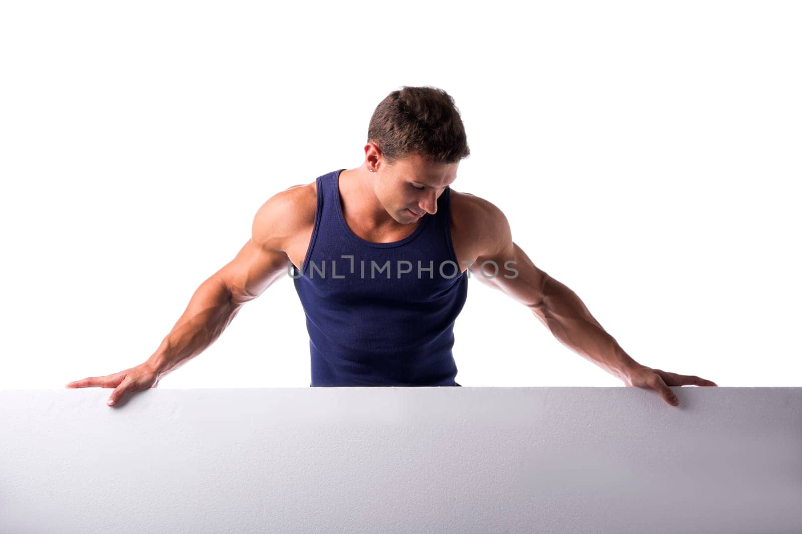 Strong muscular young man standing holding a blank horizontal white banner looking down at the copyspace for your text, on white