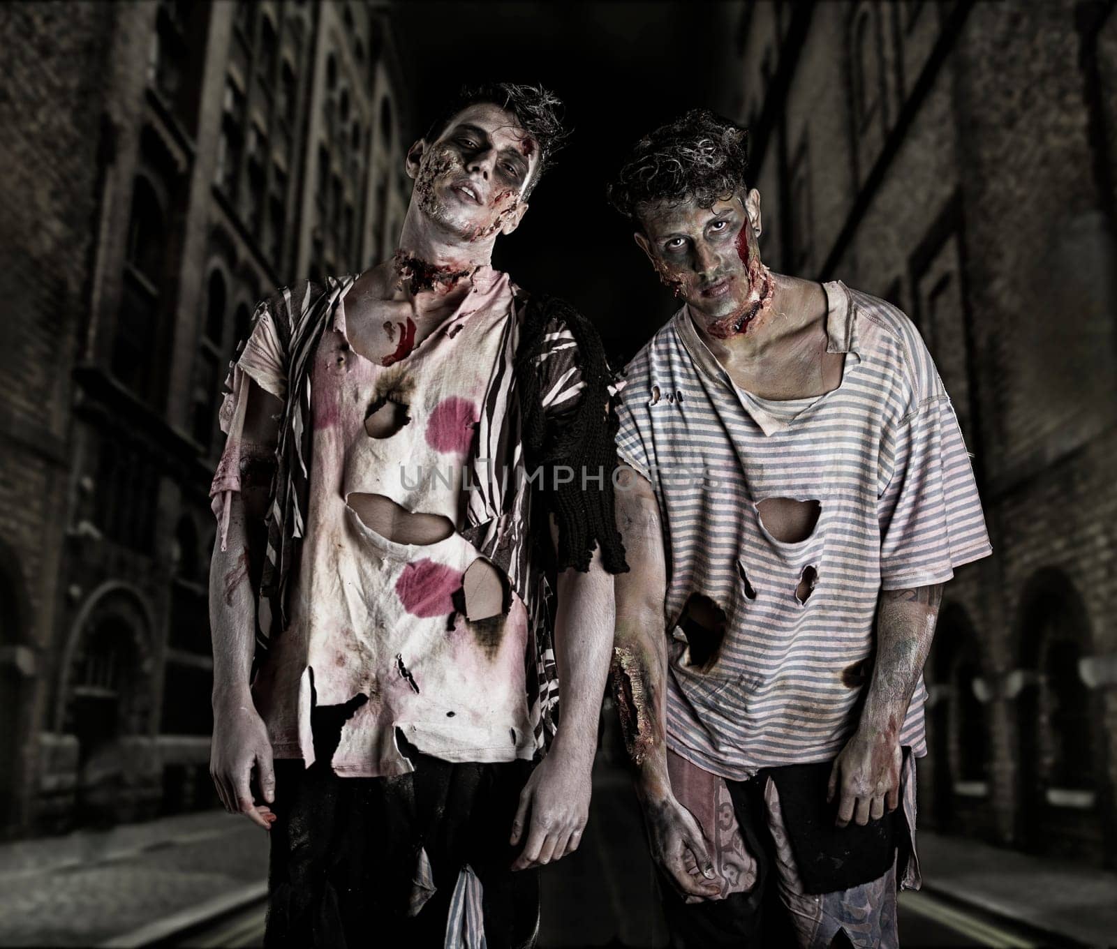 Two male zombies standing in empty city street at night looking at camera. Halloween theme