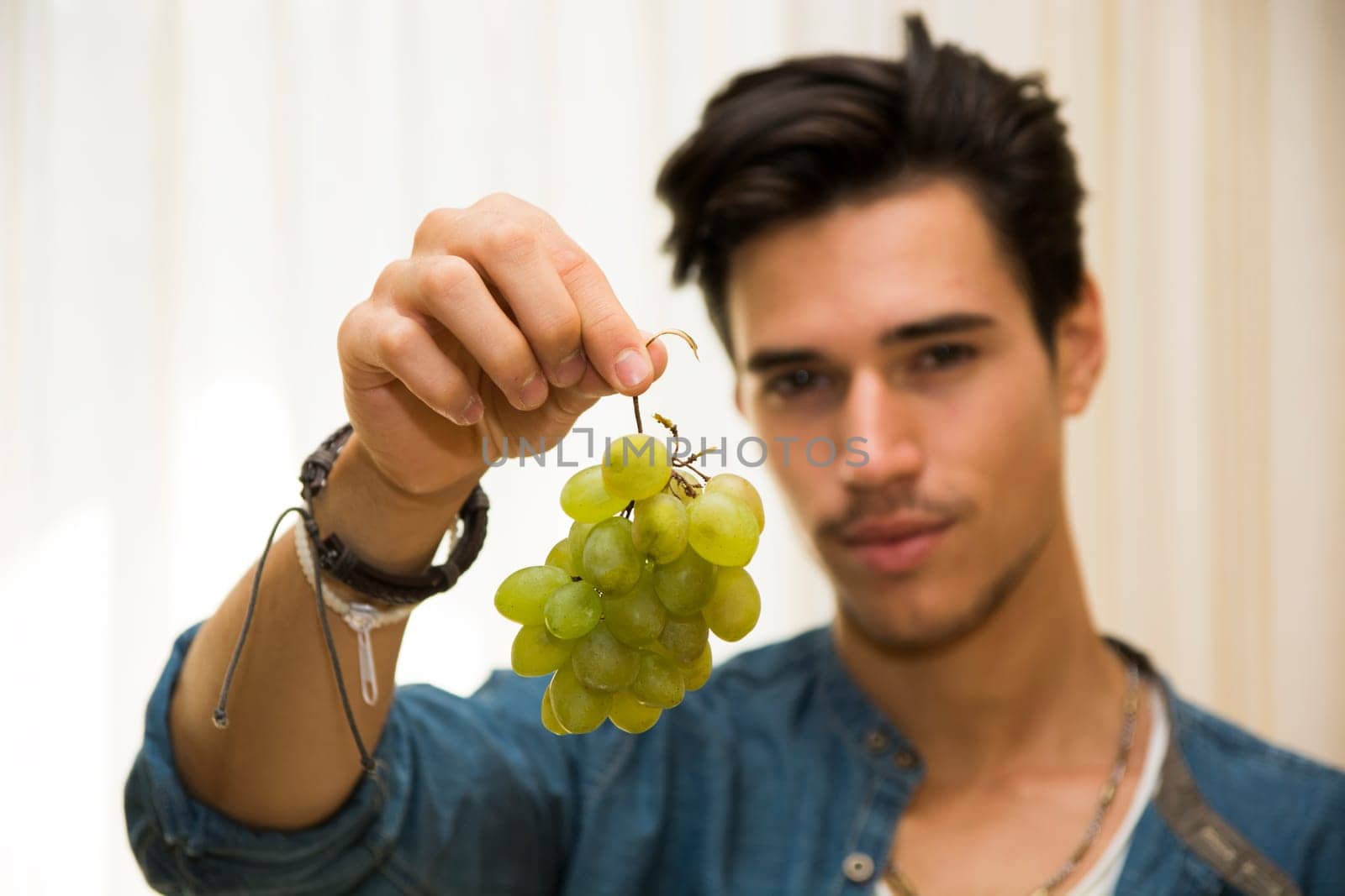 Young man holding a large delicious ripe bunch of grapes dangling from his hand, focus to the fruit