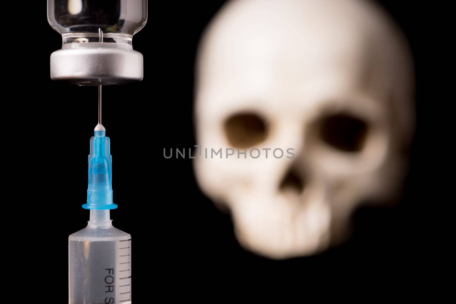 medical vials, syringe and blurry skull isolated on black background