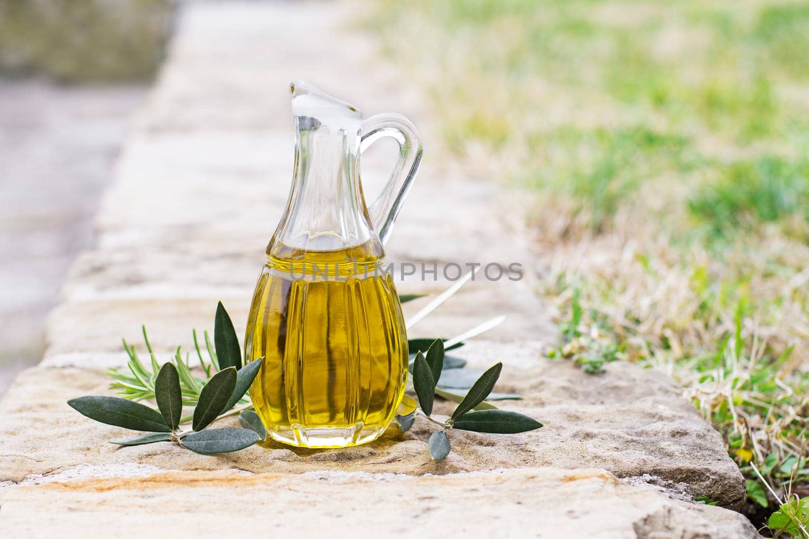 Olive oil bottle with herbs and branch in nature background