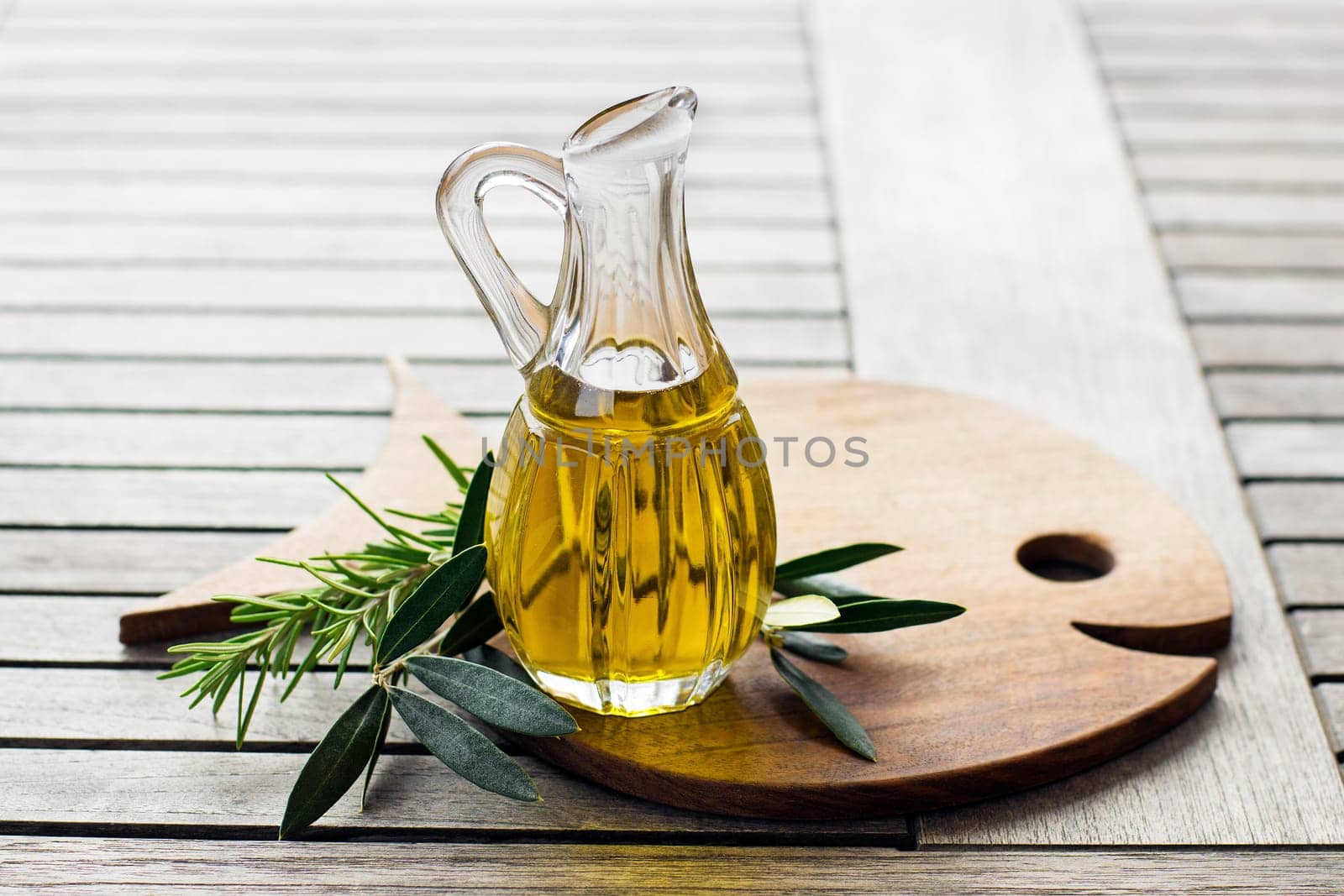 Olive oil with herbs and branch on wooden background