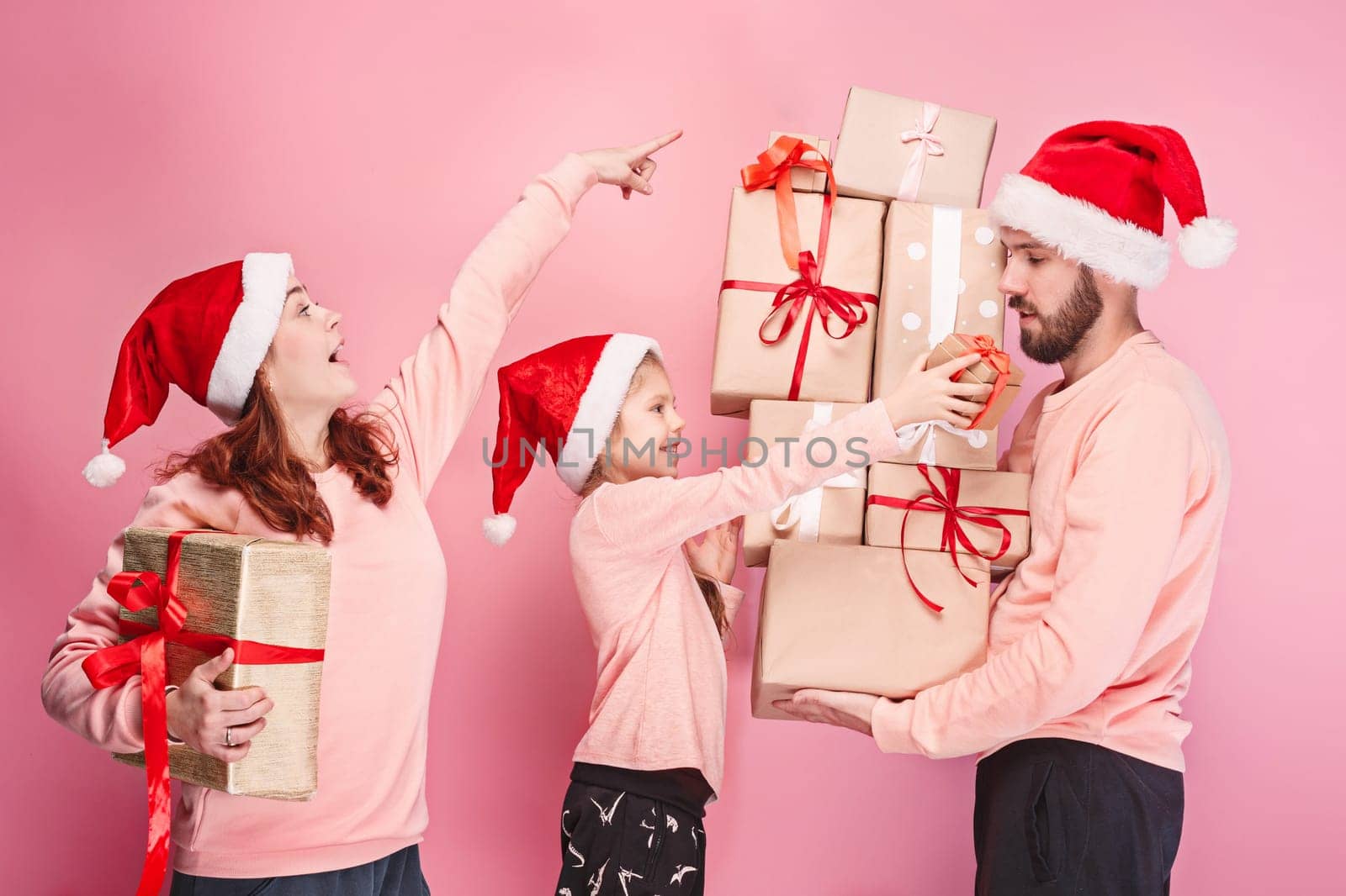 Father and mother give gifts to little daughter at pink studio background