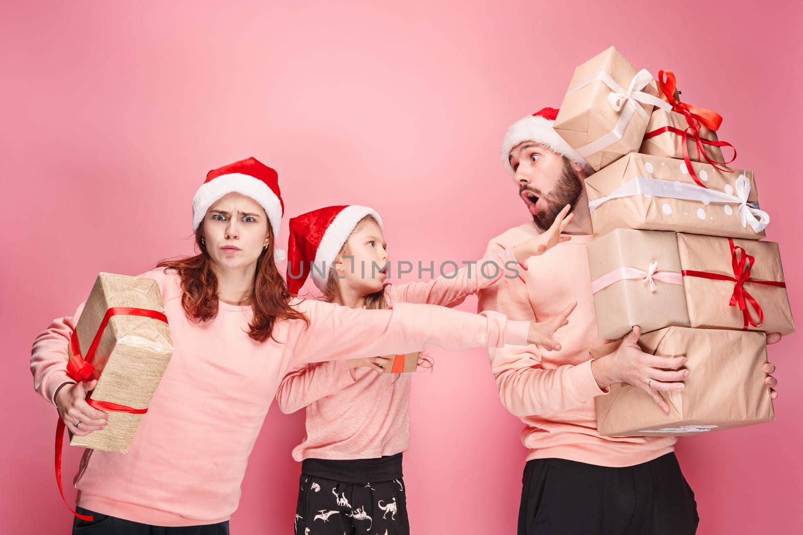 Father and mother give gifts to little daughter at pink studio background
