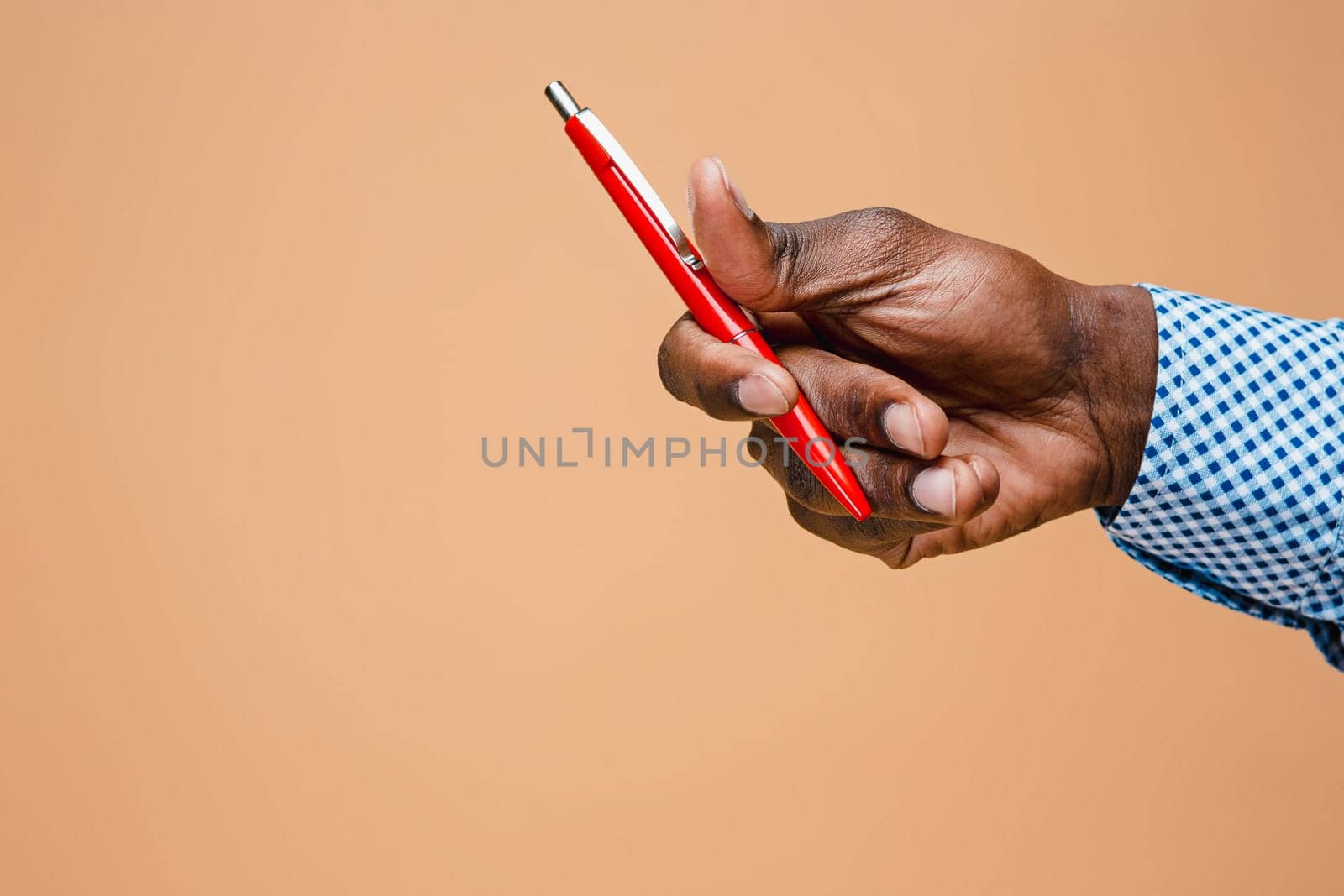 Male hand holding pencil, isolated on studio brown background