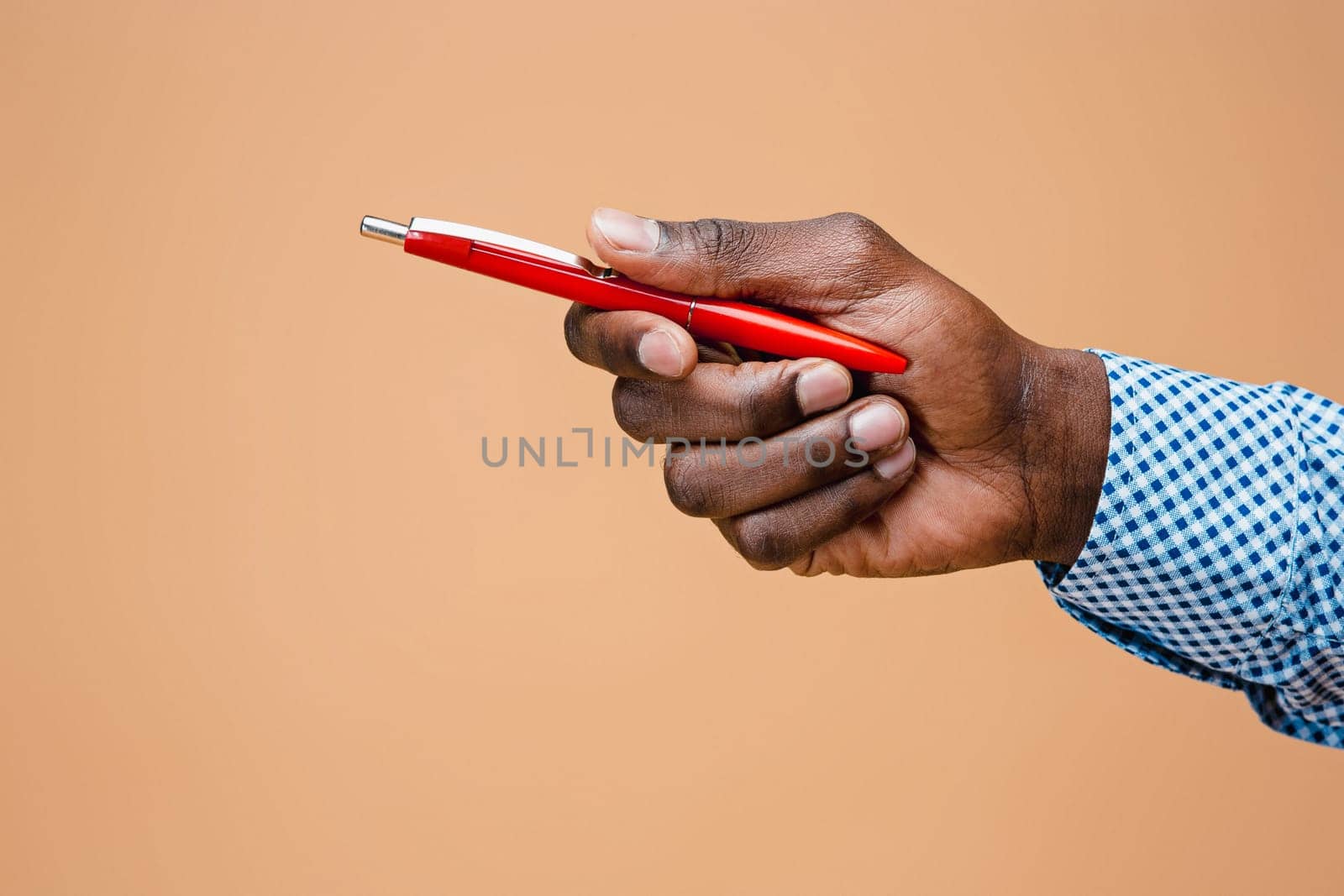 Male hand holding pencil, isolated on studio brown background