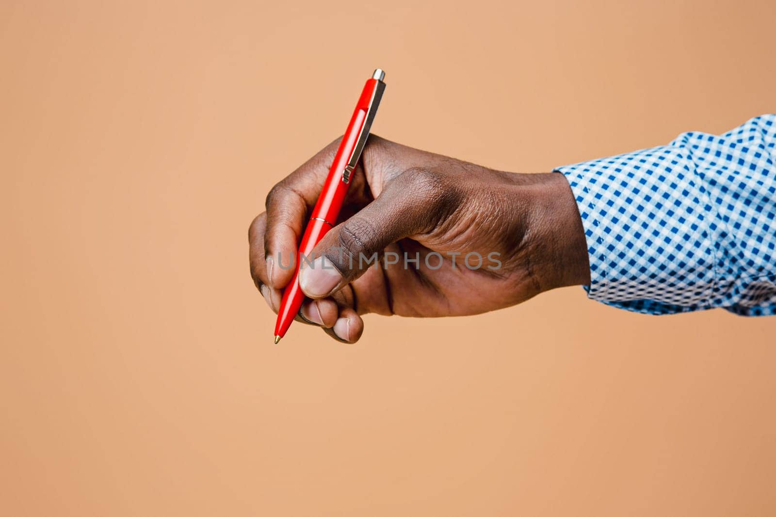 Male hand holding pencil, isolated on studio brown background