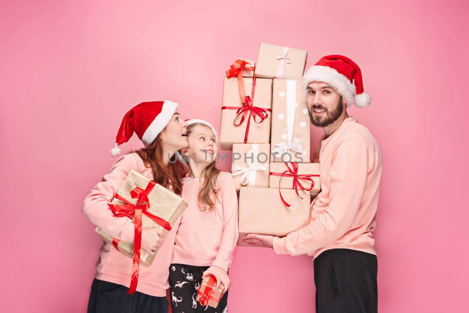 Father and mother give gifts to little daughter at pink studio background