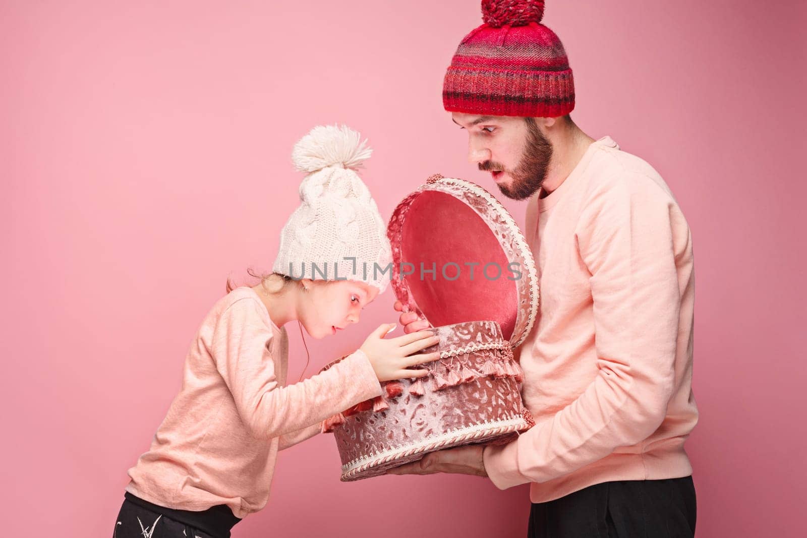 Portrait of a surprised little girl with her father holding a Christmas present at pink studio background