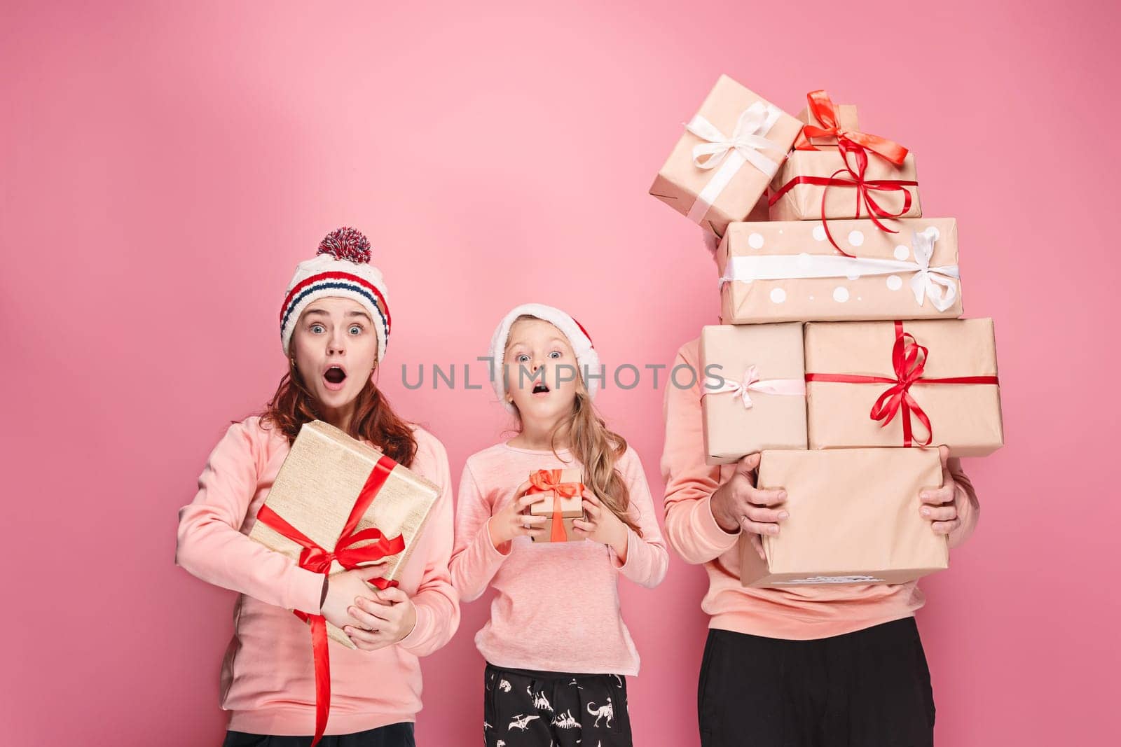 Father and mother give gifts to little daughter at pink studio background
