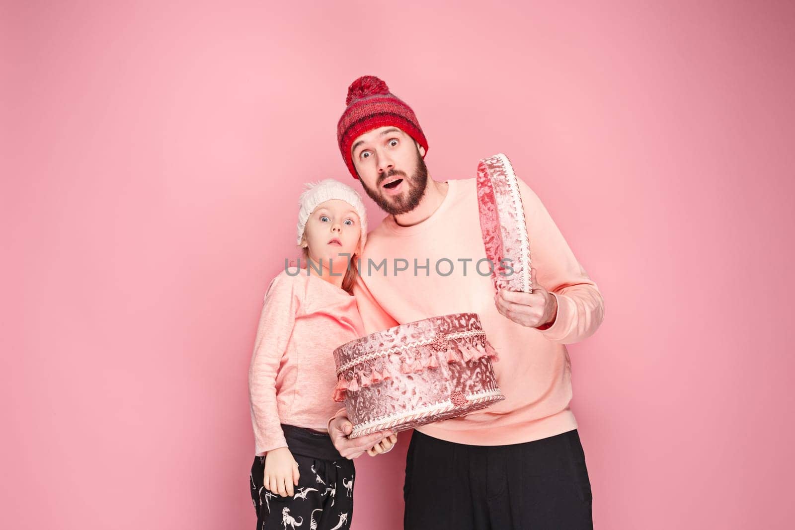 Portrait of a surprised little girl with her father holding a Christmas present at pink studio background