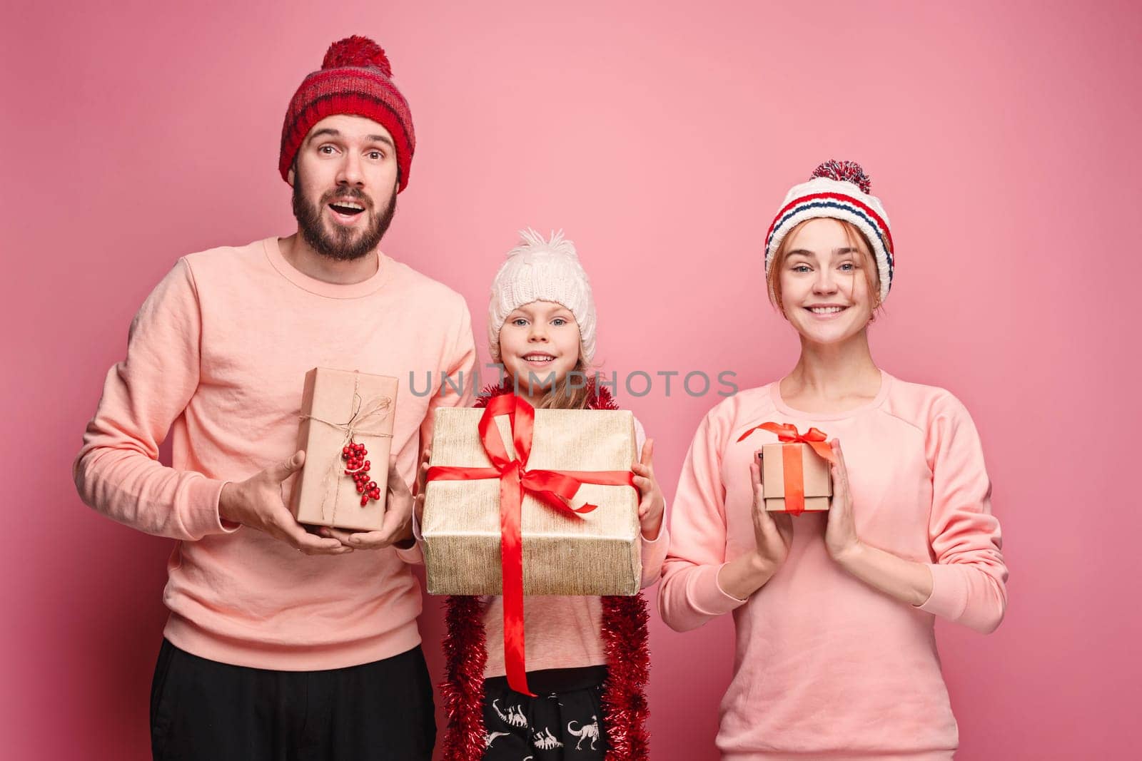 Father and mother give gifts to little daughter at pink studio background