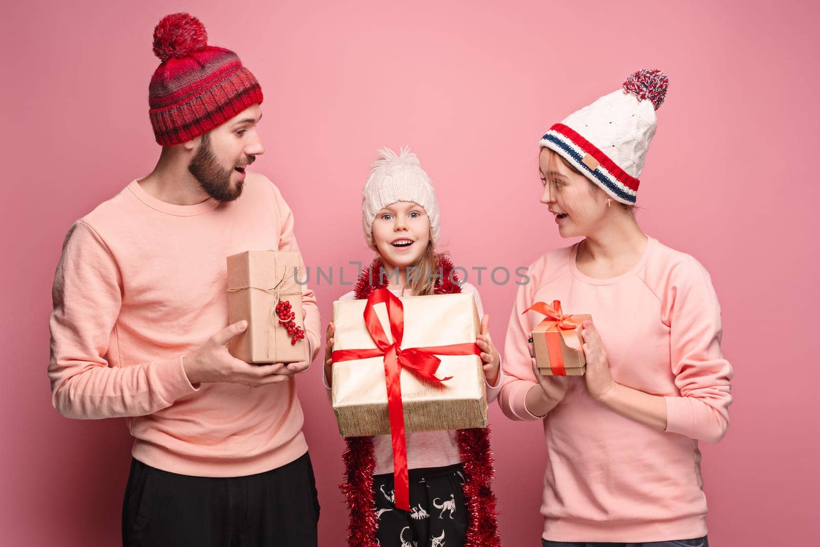 Father and mother give gifts to little daughter at pink studio background