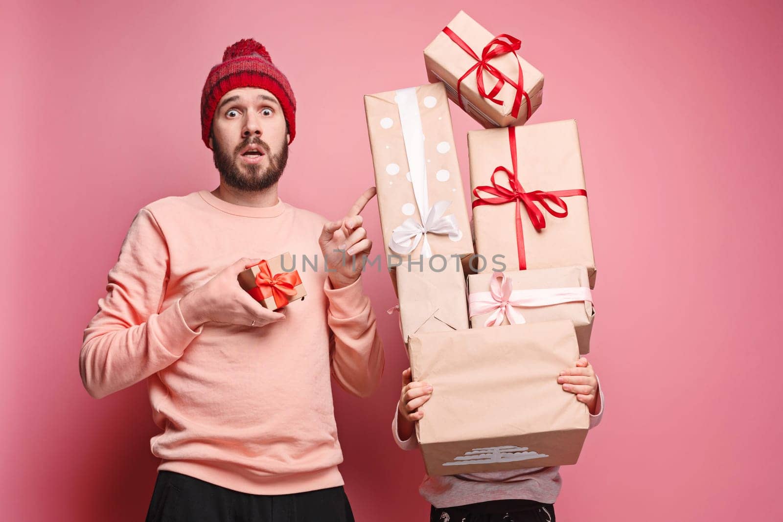 Portrait of a surprised little girl with her father holding a Christmas present at pink studio background