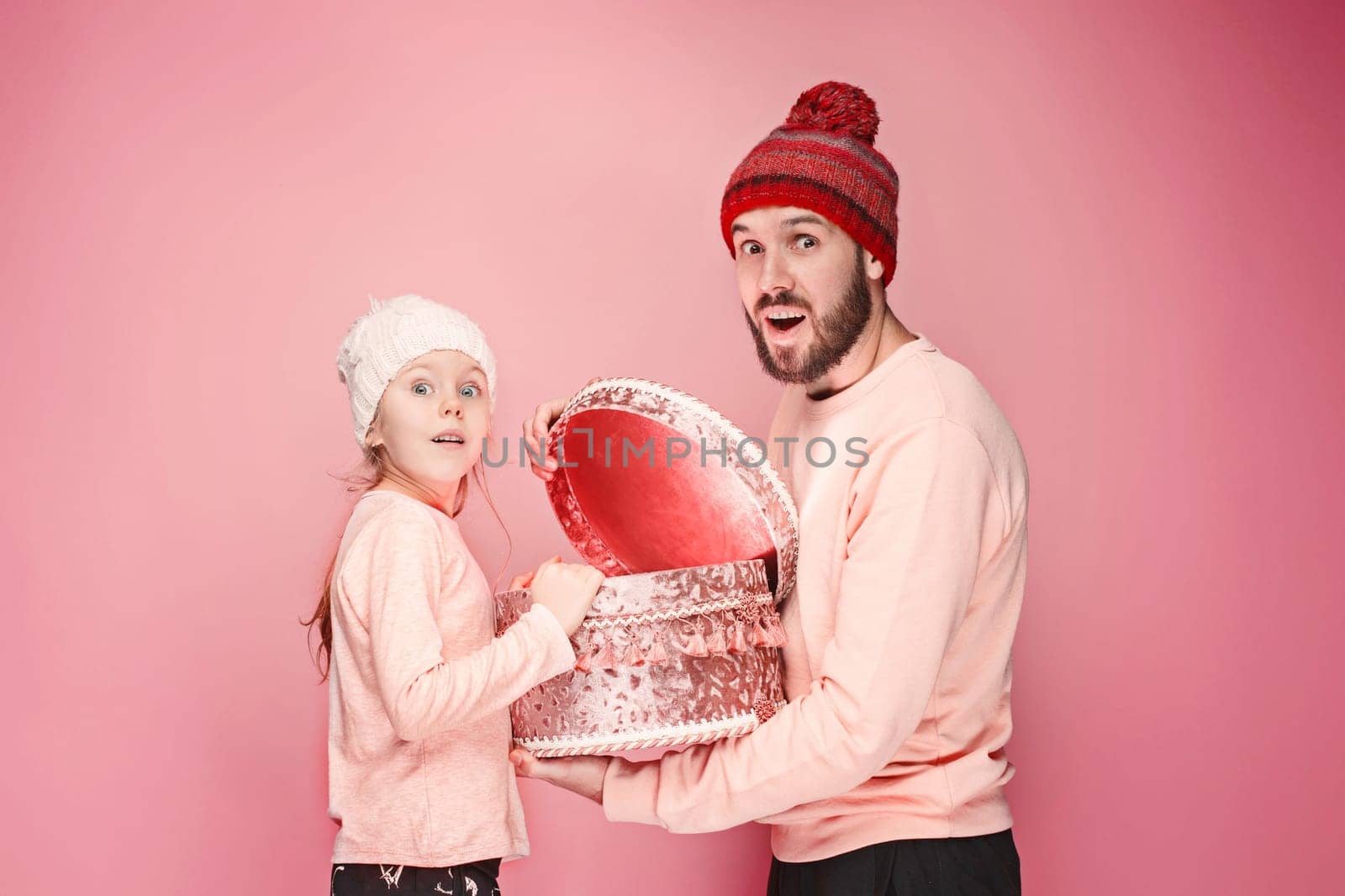 Portrait of a surprised little girl with her father holding a Christmas present at pink studio background
