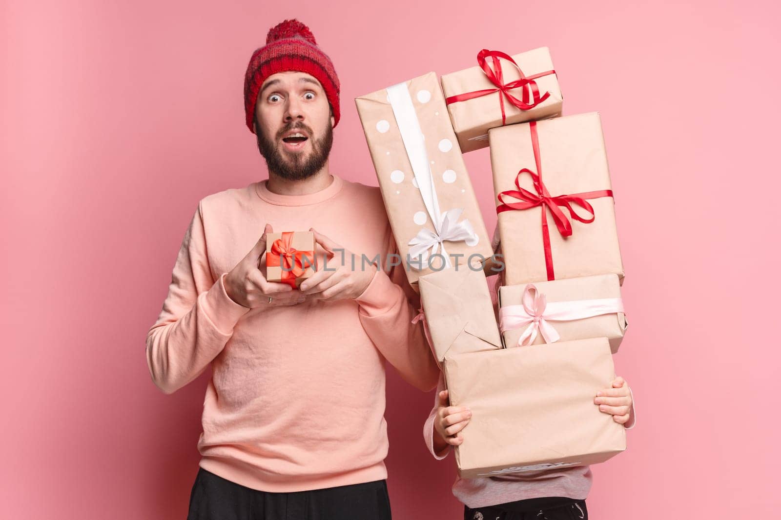 Portrait of a surprised little girl with her father holding a Christmas present at pink studio background