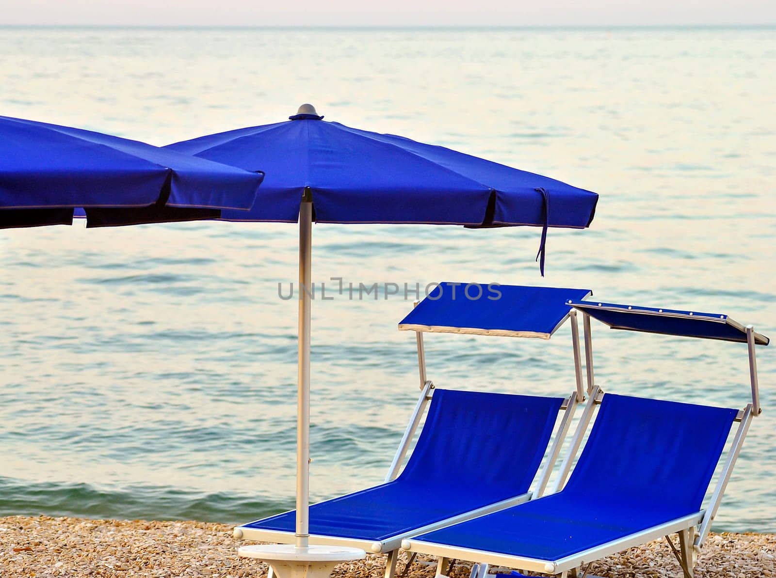 two sunbeds on a stony beach with calm sea in background