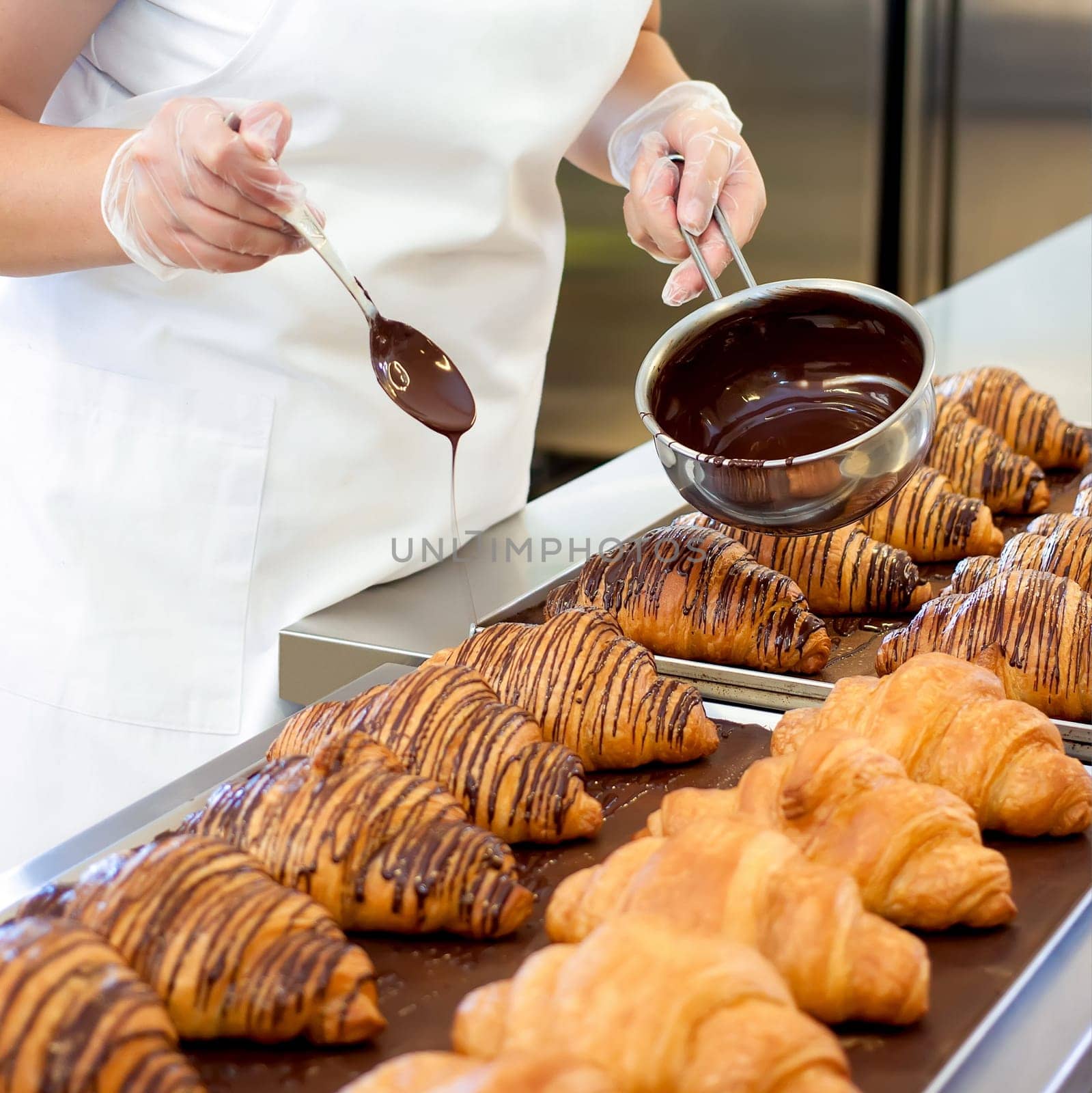 Professional chef pours chocolate over  fresh croissant