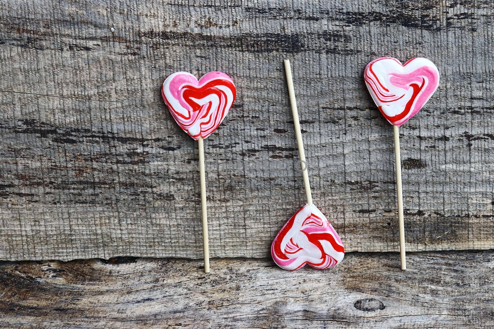 Three white-red lollipops in heart shape on a wooden background