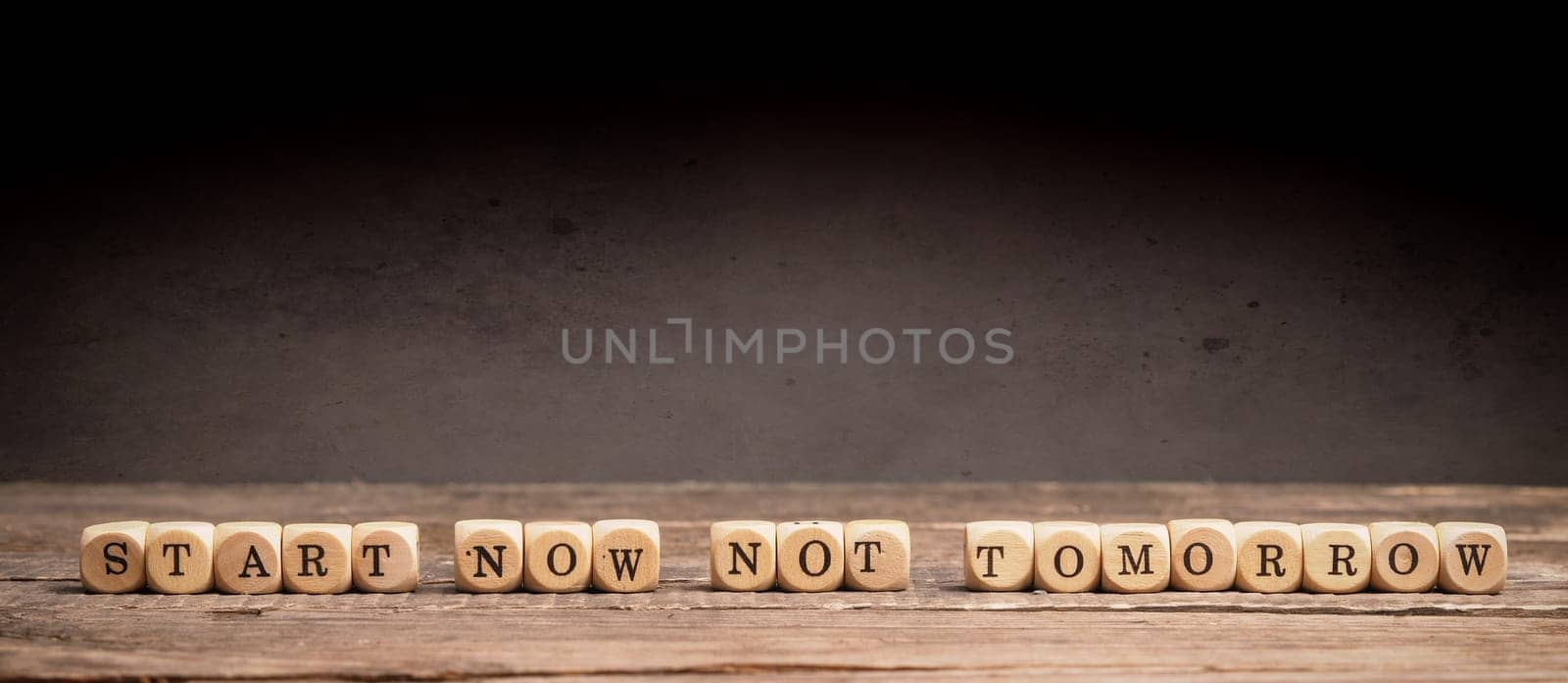 Business or New Year resolution concept with small wooden dices and the words Start now not tomorrow