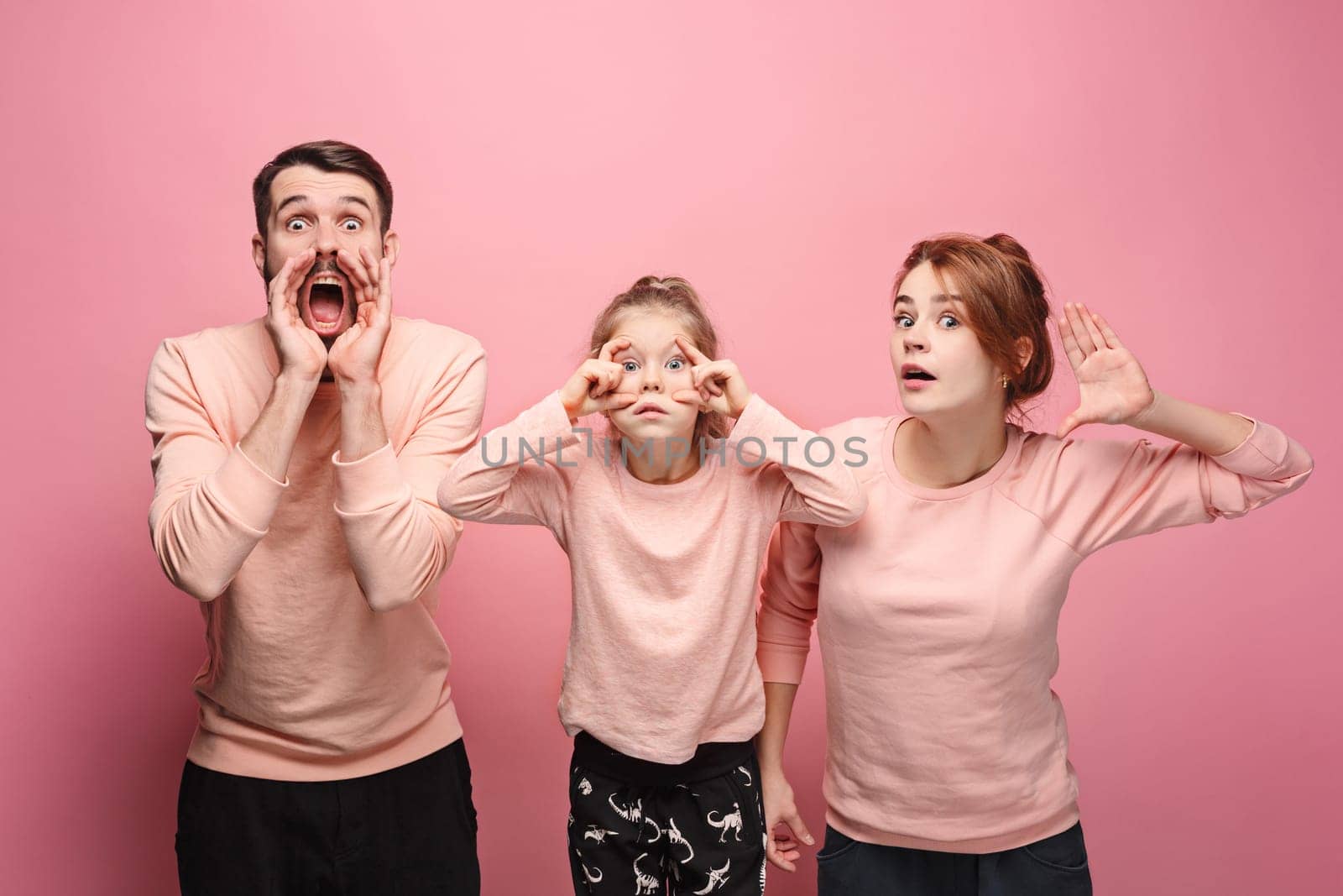 Surprised young family looking at camera on pink studio background