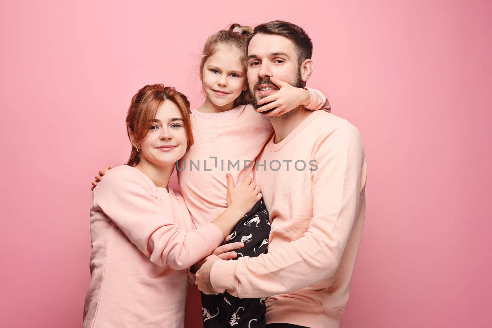 Happy young family with one little daughter posing together on pink studio background