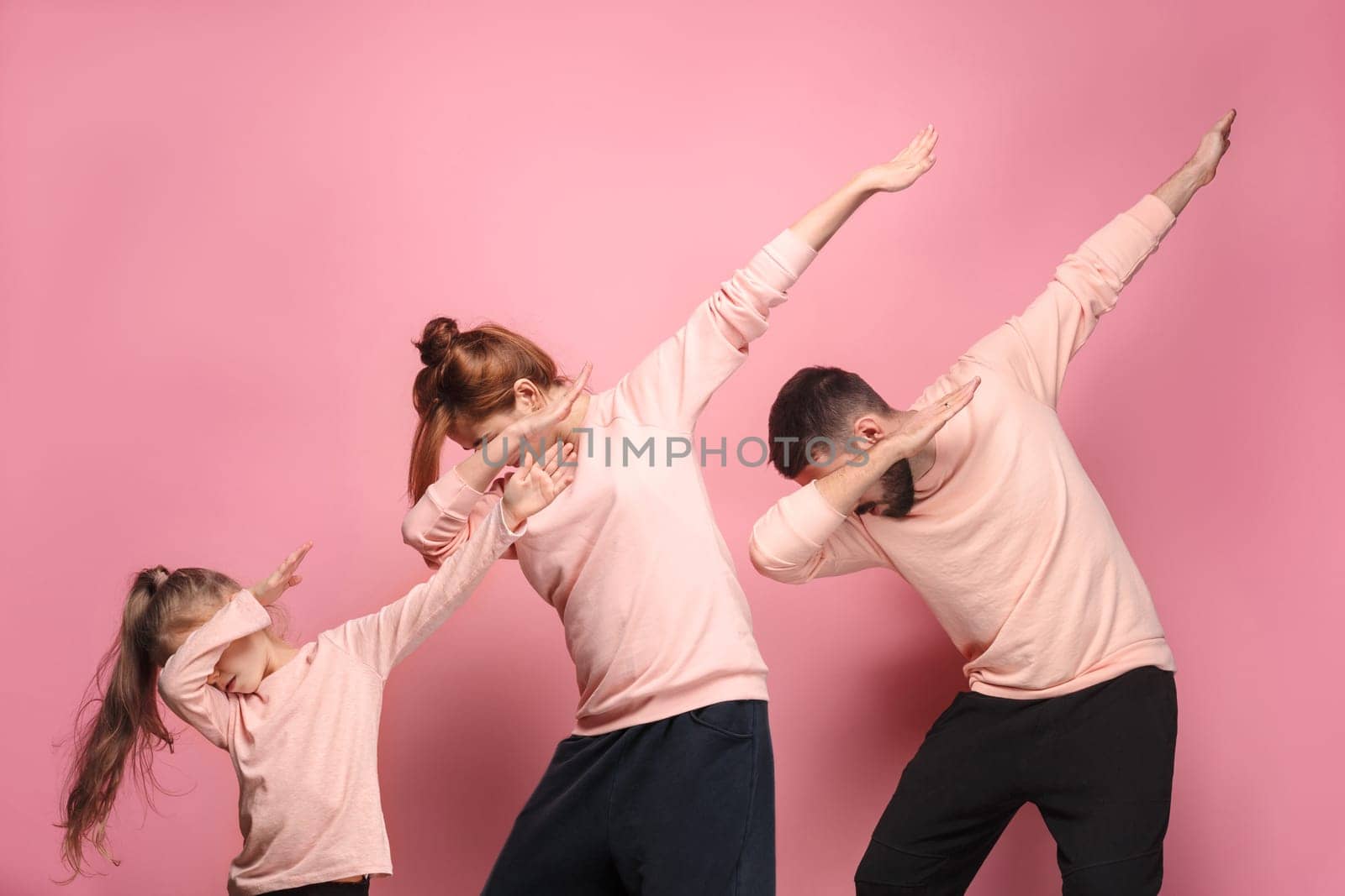The dancing young family on pink studio background